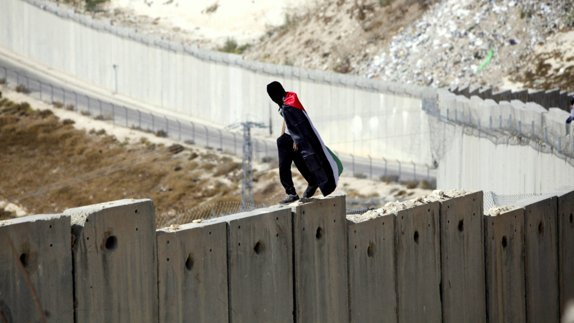 A student wrapped in a Palestinian flag walks over Israel's apartheid wall between the West Bank and Israel in Abu Dis during a protest Monday, Nov. 2, 2015. (AP Photo/Mahmoud Illean)
