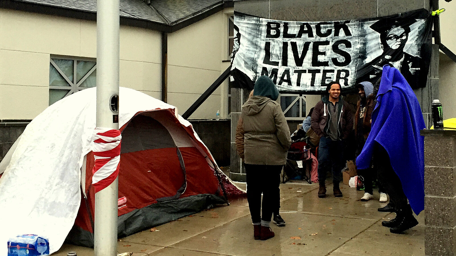 A group of protesters gather at the front entrance to the 4th Police Precinct station, Monday, Nov. 16, 2015, in Minneapolis, after a man was shot by Minneapolis police early Sunday morning. Community members and activists on Monday at a news conference demanded that police release the name of the officer involved as well as any video of the incident. (AP Photo/Kyle Potter)