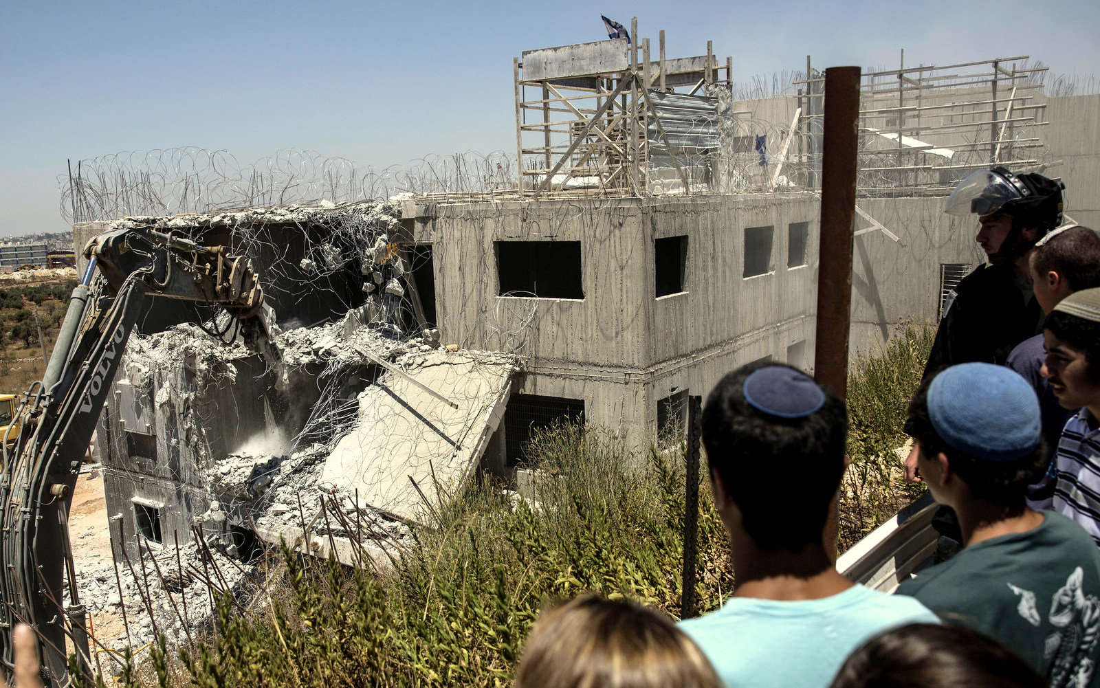 Young Israeli settlers watch the demolition of a building at the Jewish settlement of Beit El, near the West Bank town of Ramallah, Wednesday, July 29, 2015. Israeli bulldozers began demolishing a contested housing complex in a West Bank settlement on Wednesday as the prime minister’s office announced the “immediate construction” of some 300 new units at another location in the same settlement and advanced plans for about 500 new units in east Jerusalem. (AP Photo/Tsafrir Abayov)
