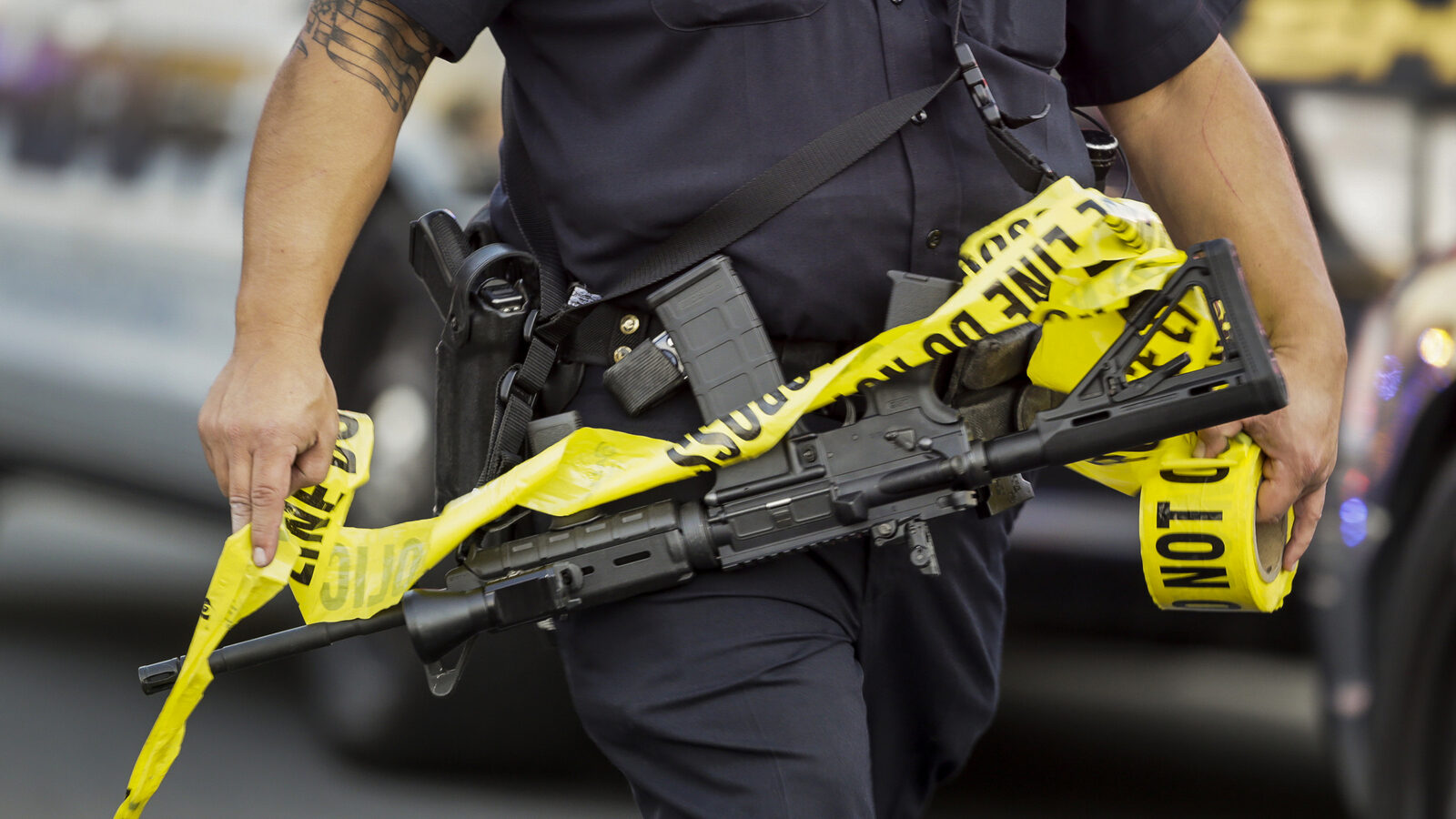 A police officer deploys tape to an area near where attackers opened fire on a banquet at a social services center for the disabled in San Bernardino. (AP Photo/Damian Dovarganes)