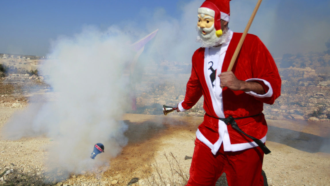 Santa dodges a tear gas canister fired by Israeli troops during a protest against Israel's apartheid wall, help MintPress dodge corruption and corporate media, donate today! (AP Photo/Majdi Mohammed)