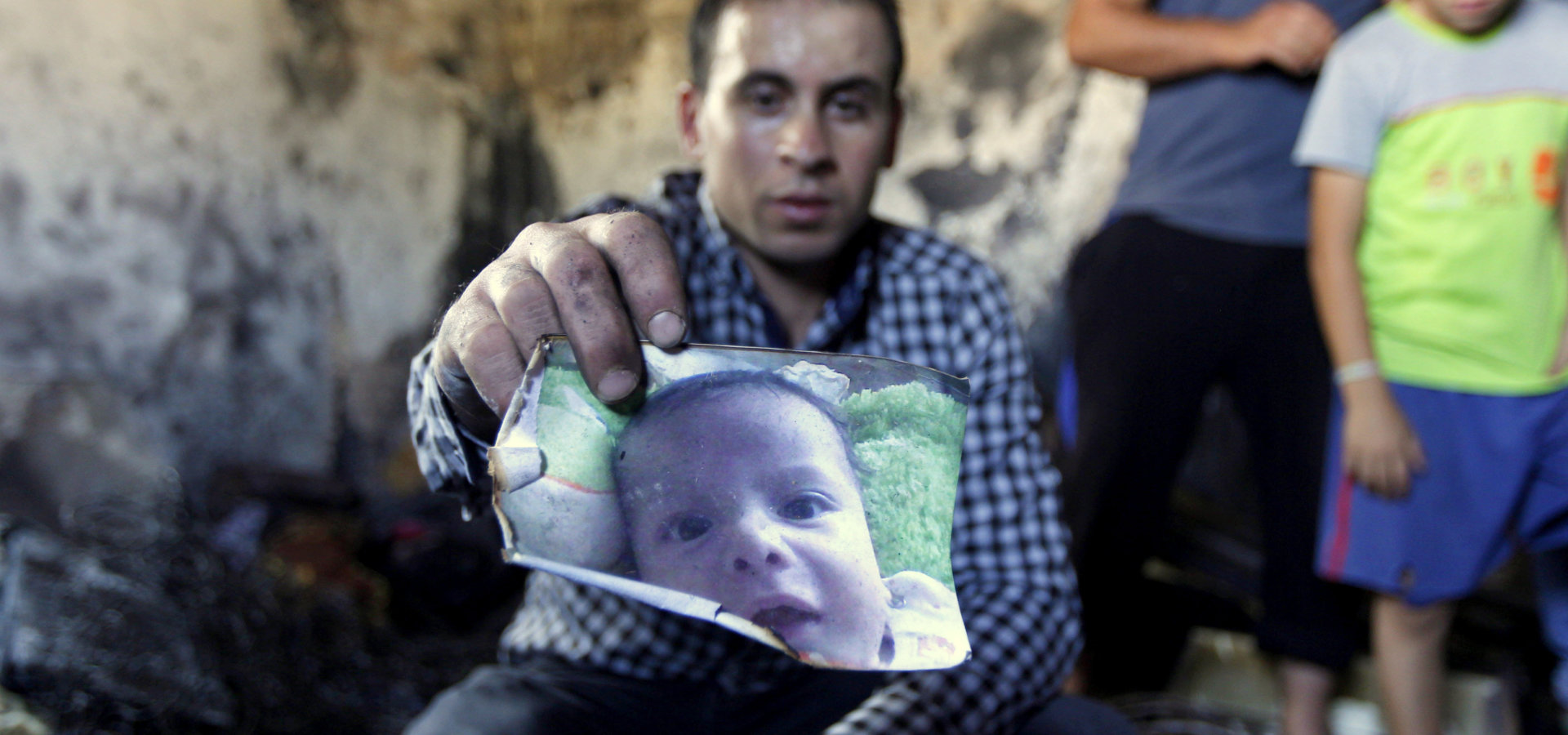 A relative holds up a photo of a one-and-a-half year old boy, Ali Dawabsheh, killed in a house that had been torched in an attack by Jewish extremists in Duma village near the West Bank city of Nablus, Friday, July 31, 2015. (AP Photo/Majdi Mohammed)