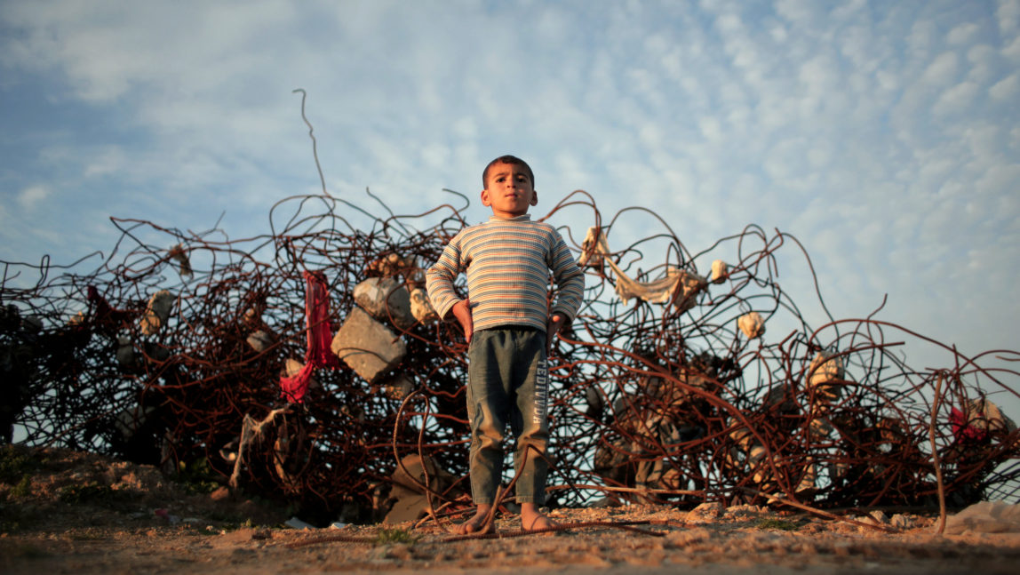 A Palestinian barefoot boy stands next to remains of a destroyed house in the town of Beit Hanoun, northern Gaza Strip, Monday, Jan. 4, 2016. (AP Photo/ Khalil Hamra)
