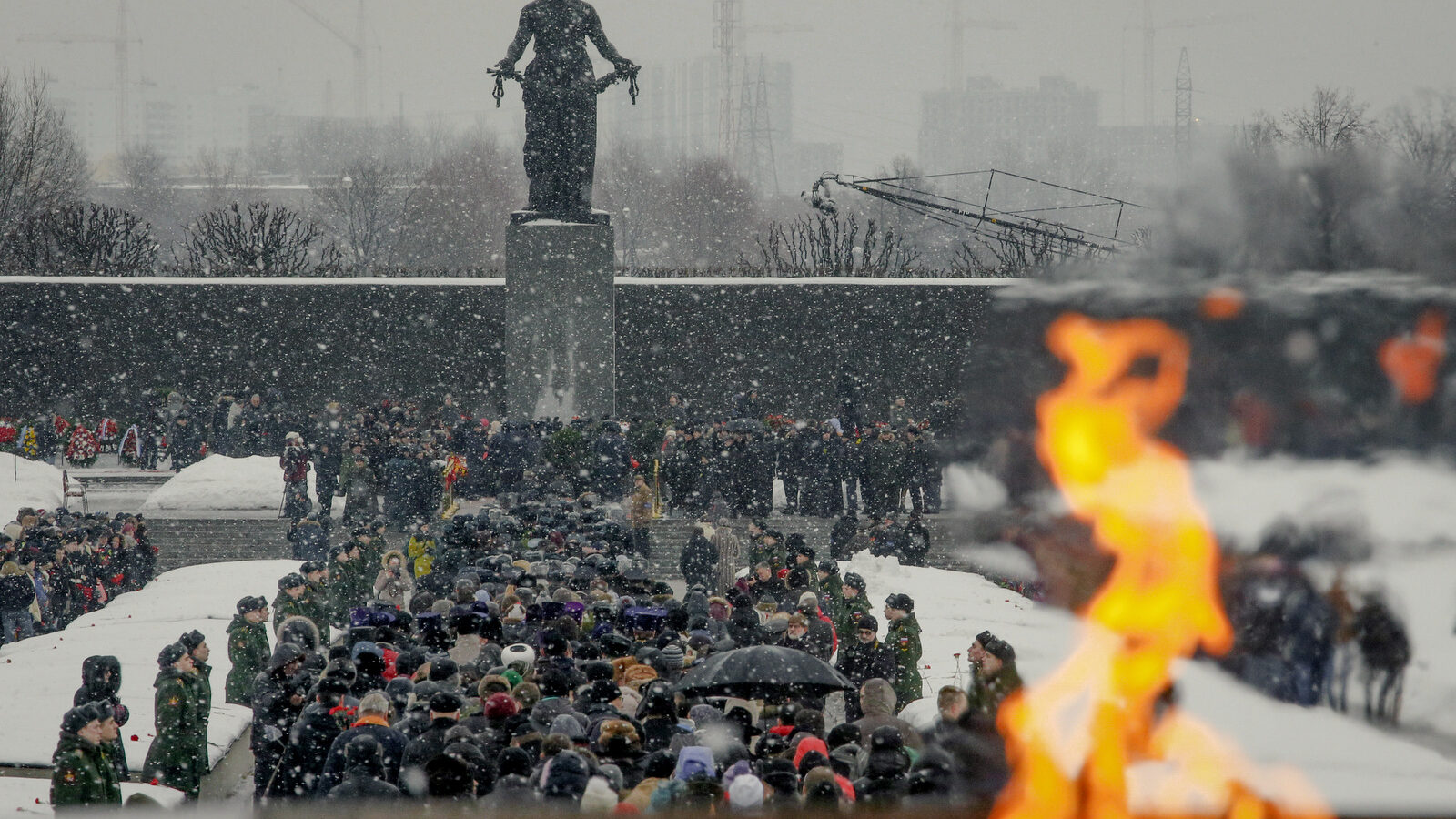 People walk in snowfall from an eternal flame to the Motherland monument to put flowers at the Piskaryovskoye Cemetery