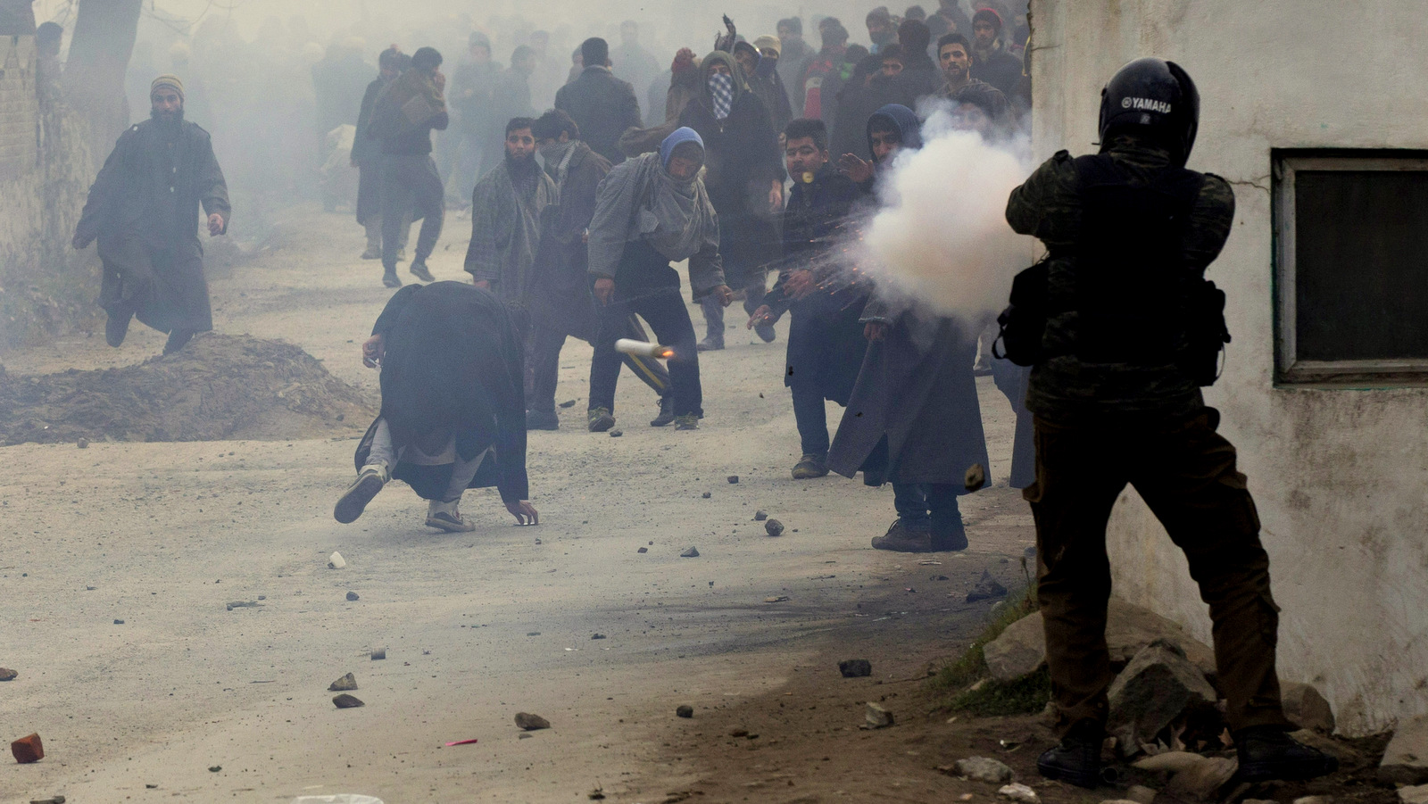 An Indian policeman fires a teargas shell as a Kashmiri Muslim, center, ducks to avoid it during the funeral procession of Sajad Ahmed Bhat, a top rebel commander on the outskirts of Srinagar, Indian controlled Kashmir, Tuesday, Jan. 12, 2016. Clashes erupted in Indian-controlled Kashmir Tuesday as police fired tear gas to stop a march by thousands of people participating in a funeral procession of a local militant killed in a gunfight with government forces. (AP Photo/Dar Yasin)