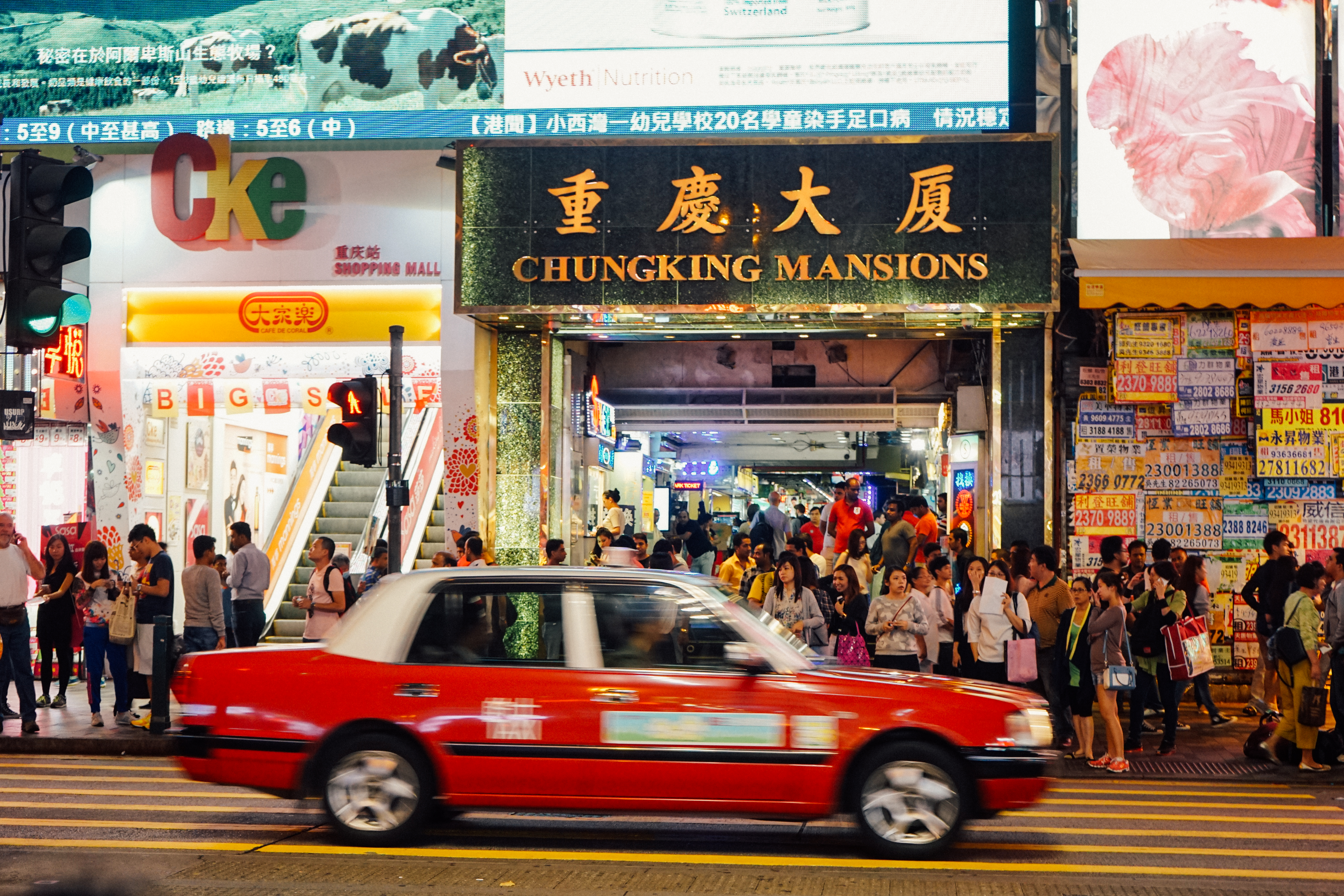  A red taxi drives past tthe busy exterior of the Chungking Mansions in Hong Kong. These squalid, overcrowded towers house many of the territory's 10,000 asylum seekers. (Shadowproof / Zachary Senn)