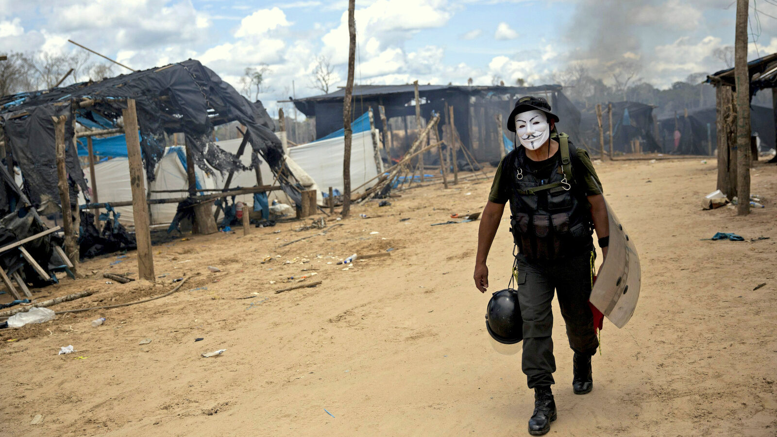 In this Wednesday, Feb. 24, 2016 photo, a police officer sports a Guy Fawkes mask he confiscated during continued government raids on illegal wildcat gold mining operations in La Pampa, in Peru's Madre de Dios region. More than 1,000 police and soldiers dynamited and dismantled mining machinery valued at $3 million, including dredges and motors used to separate gold flecks from sand in crude sluices, the government said. (AP Photo/Rodrigo Abd)