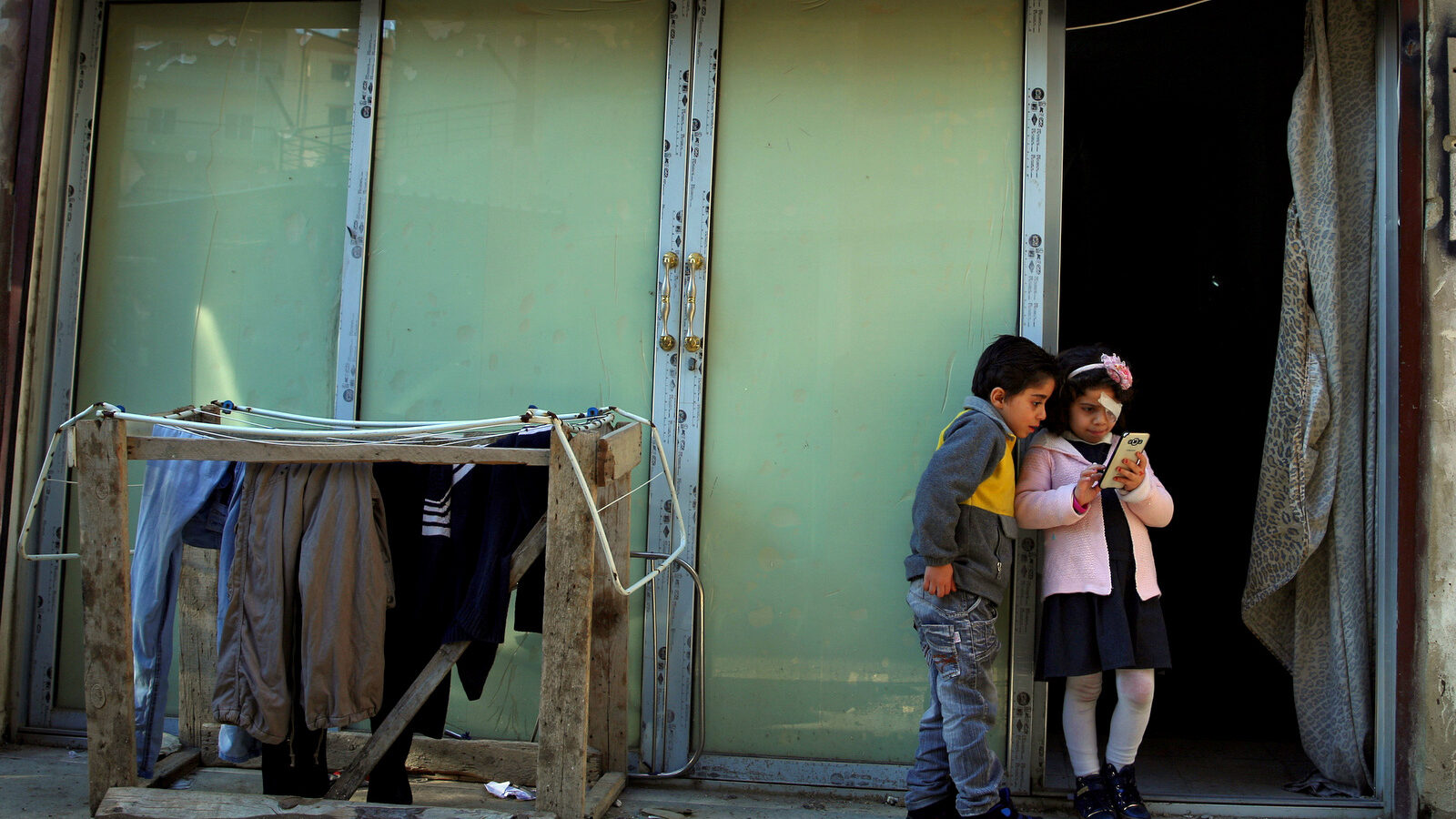 In this Tuesday, Feb. 2, 2016 photo, Syrian refugee Falak al Hourani, 7, right, and her brother Hussein Hourani, 6, who fled with their family from Homs in Syria, stand at the entrance to a shop that has been turned into a home, in the northern city of Tripoli, Lebanon. Falak, suffering from a rare form of eye cancer arrived in Italy on Thursday, the first of an estimated 1,000 refugees who are being brought here on humanitarian grounds in a pilot project aimed at dissuading people from embarking on deadly sea crossings. (AP Photo/Bilal Hussein)