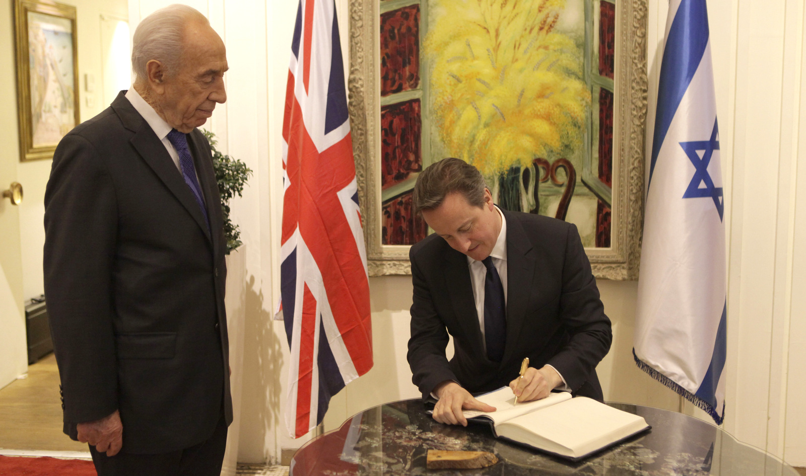 Former Israeli President Shimon Peres watches as British Prime Minister David Cameron signs a visitors book in Jerusalem Wednesday, March 12, 2014. Cameron was visiting  Israel to vow support in rejecting boycott attempts against the Jewish state. (AP Photo/Dan Balilty)