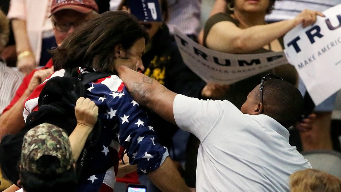 Trump protester Bryan Sanders, center left, is punched by a Trump supporter as he is escorted out of Republican presidential candidate Donald Trump's rally at the Tucson Arena in downtown Tucson, Ariz., Saturday, March 19, 2016. (Mike Christy/Arizona Daily Star via AP) MANDATORY CREDIT