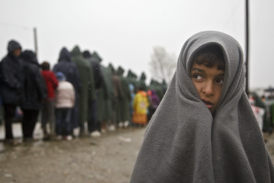 Migrant child covered in blanket stands in rain at the Greek border camp near Idomeni, Thursday, March 10, 2016. Northbound borders are closed and authorities plan to distribute fliers telling refugees seeking to reach central Europe that there is no hope of you continuing north, therefore come to the camps where we can provide assistance as more than 36,000 transient migrants are thought to be stuck in financially struggling Greece. (AP Photo/Visar Kryeziu)