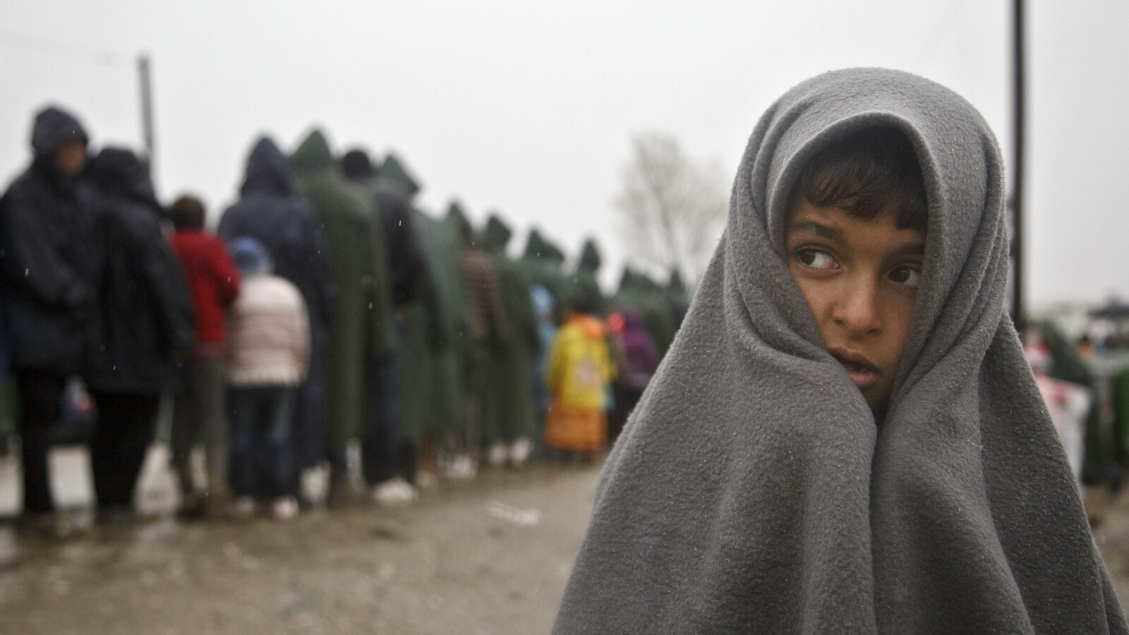 Migrant child covered in blanket stands in rain at the Greek border camp near Idomeni, Thursday, March 10, 2016. Northbound borders are closed and authorities plan to distribute fliers telling refugees seeking to reach central Europe that there is no hope of you continuing north, therefore come to the camps where we can provide assistance as more than 36,000 transient migrants are thought to be stuck in financially struggling Greece. (AP Photo/Visar Kryeziu)