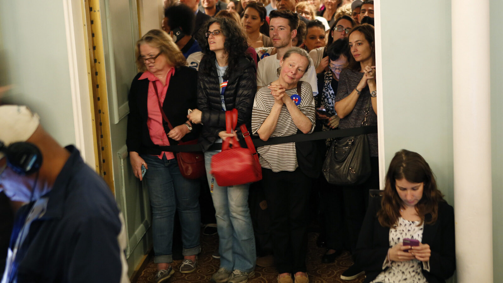 Hillary Clinton supporters who couldn't get into a Women for Hillary event listen and watch from behind a press riser in the back of a ballroom, as Democratic presidential candidate Hillary Clinton speaks during a campaign stop a day ahead of the New York primary, Monday, April 18, 2016, in New York. (AP Photo/Kathy Willens)