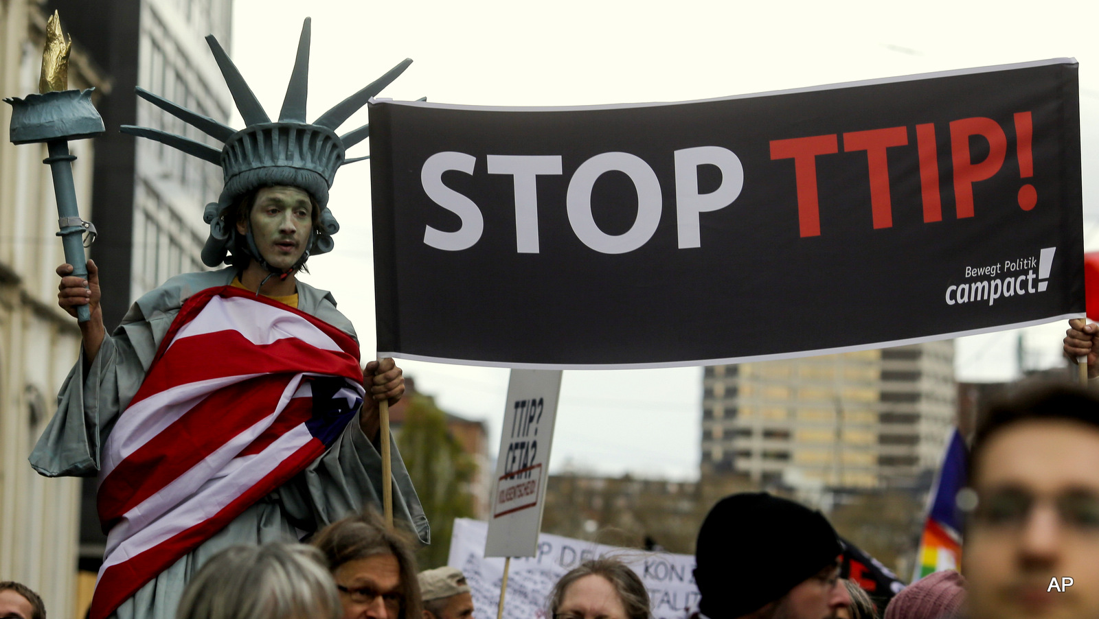 A man on stilts and dressed like the Statue of Liberty holds a banner with the slogan Stop TTIP during a protest of thousands of demonstrators against the planned Transatlantic Trade and Investment Partnership, TTIP, and the Comprehensive Economic and Trade Agreement, CETA, ahead of the visit of United States President Barack Obama in Hannover, Germany, Saturday, April 23, 2016.