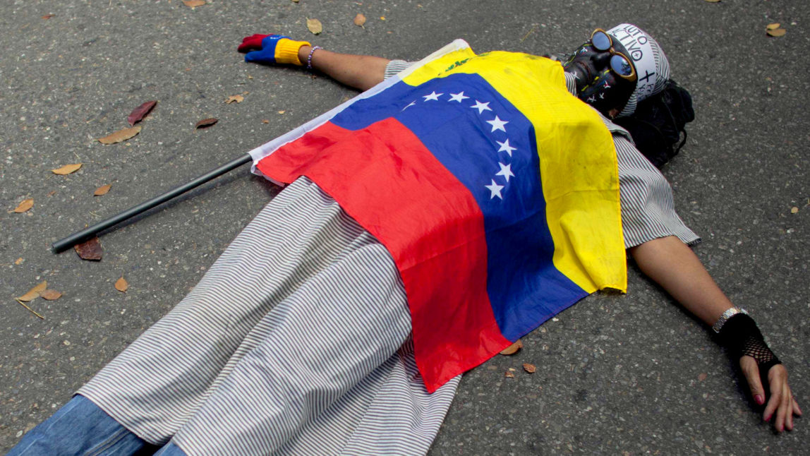 A protester covered by the Venezuelan flag lies on the ground during a protest against violence outside the Vatican's diplomatic mission in Caracas, Venezuela, Wednesday, Feb. 25, 2015. (AP Photo/Ariana Cubillos)