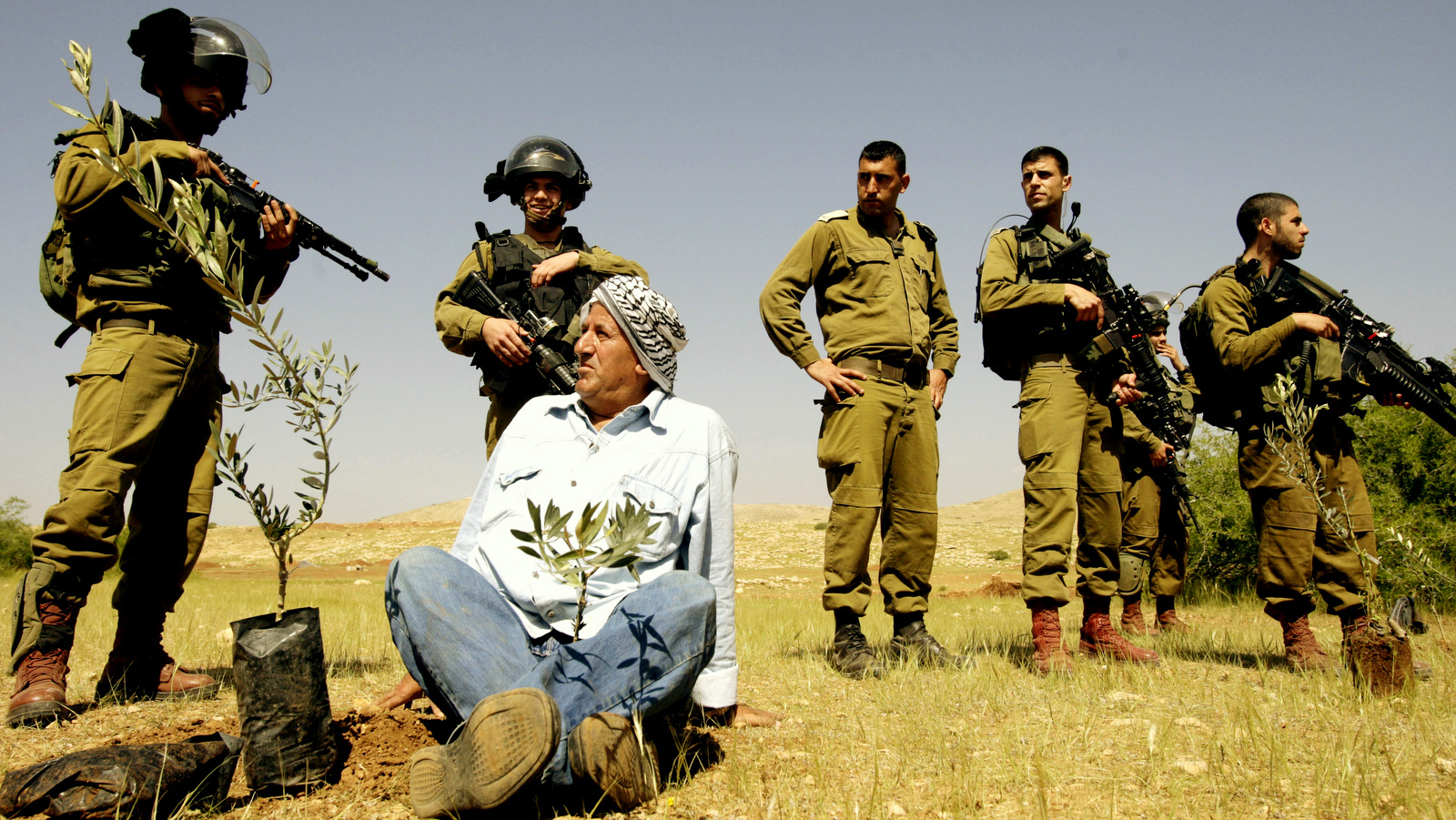 A Palestinian farmer looks at Israeli army soldiers after he planted an olive trees near the West Bank town of Tubas in the Jordan valley, during a protest against the closure of land to Palestinians by the army and Jewish settlers, Tuesday, April 8, 2014. (AP/Mohammed Ballas)