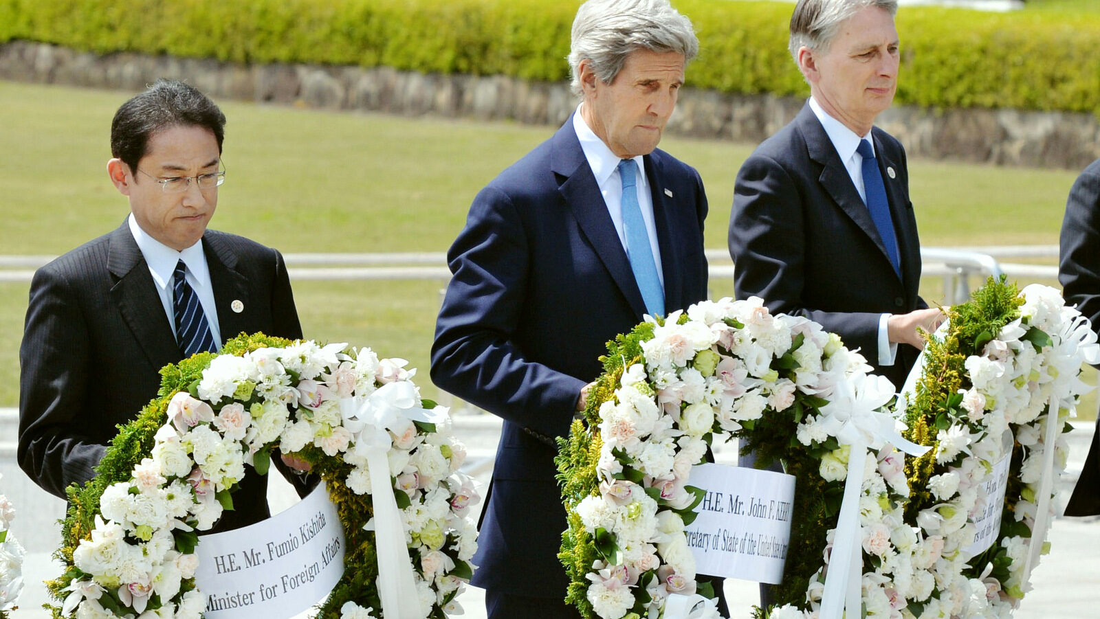 From left, Japan's Foreign Minister Fumio Kishida, U.S. Secretary of State John Kerry and Britain's Foreign Minister Philip Hammond carry wreath to offer at the cenotaph at Hiroshima Peace Memorial Park in Hiroshima, western Japan Monday, April 11, 2016. (Kyodo News via AP)