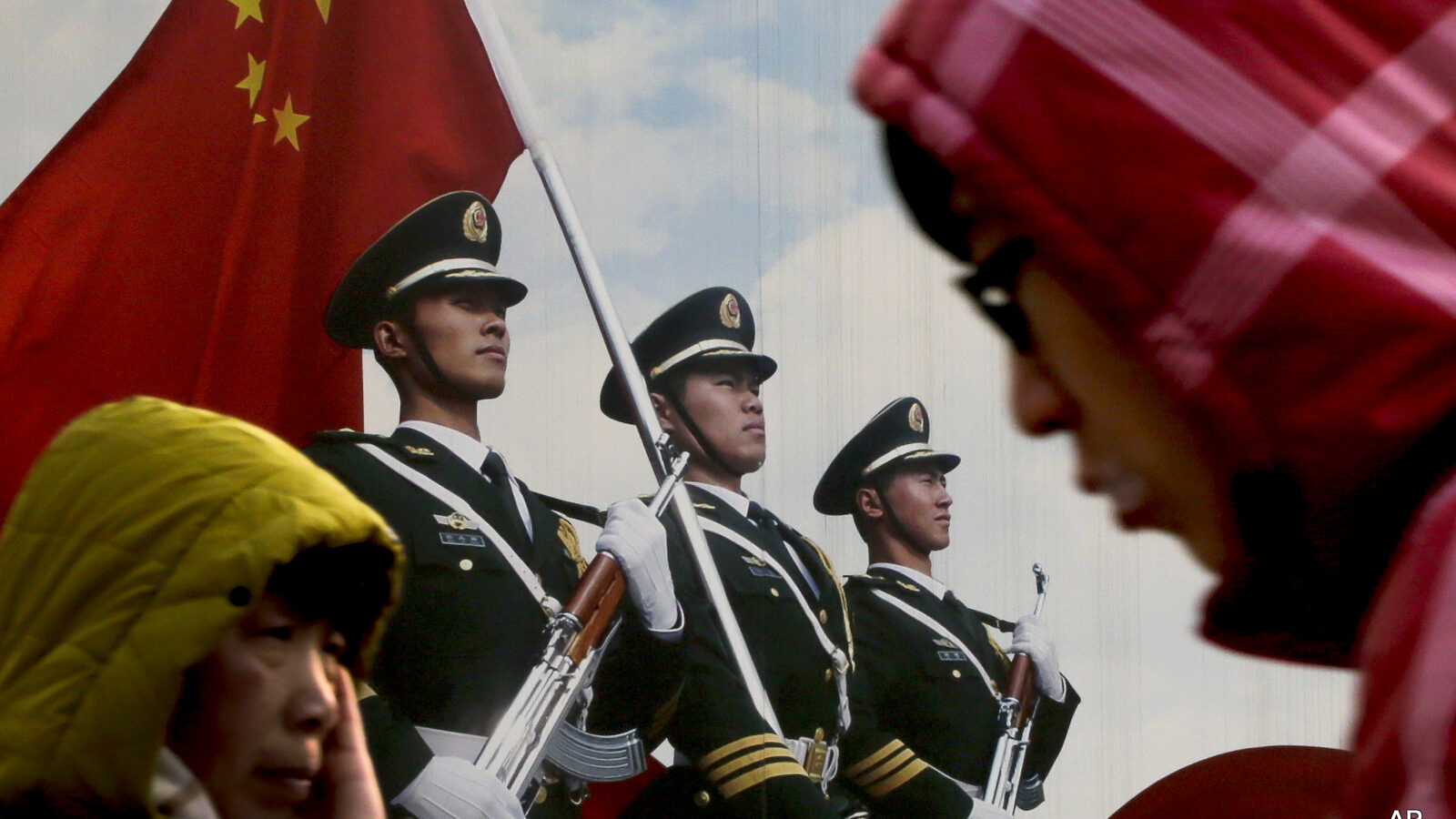 People walk past a poster of Chinese People's Liberation Army (PLA) soldiers on display in Beijing, Thursday, Jan. 21, 2016