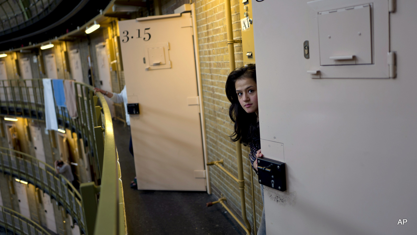 In this Saturday, May 7, 2016 photo, Afghan refugee Shazia Lutfi, 19, peeks through the door of her cell at the former prison of De Koepel in Haarlem, Netherlands. The government has let Belgium and Norway put prisoners in its empty cells and now, amid the huge flow of migrants into Europe, several Dutch prisons have been temporarily pressed into service as asylum seeker centers.