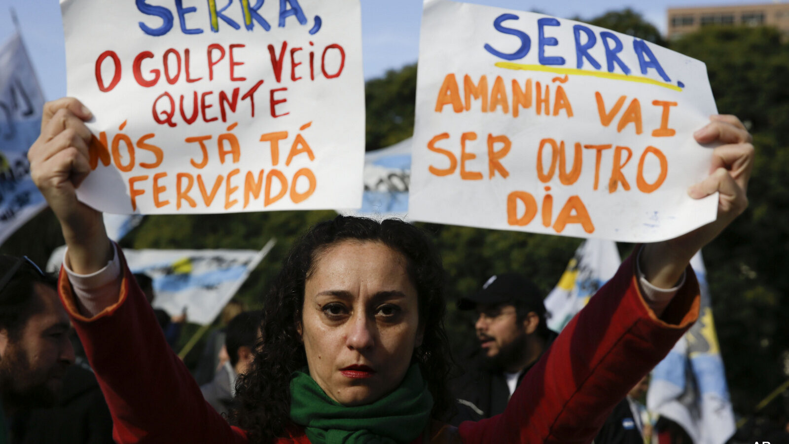 A woman holds up signs that say in Portuguese "Serra, the coup is hot, we're already boiling," left, and "Serra, tomorrow will be another day" as protesters wait for him outside the Foreign Relations Ministry where he'll meet Argentina's Foreign Minister Susana Malcorra in Buenos Aires, Argentina, Monday, May 23, 2016. Serra is on his first state visit since being appointed in the wake of Brazilian President Dilma Rousseff's impeachment. (AP Photo/Natacha Pisarenko)