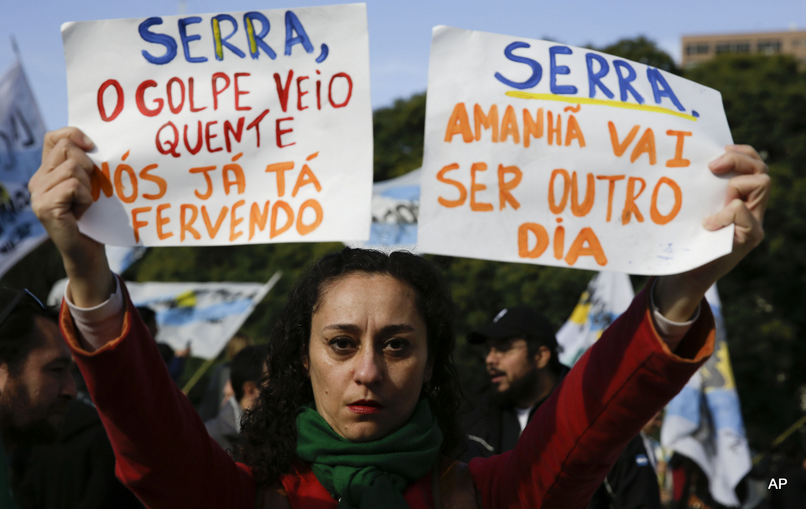 A woman holds up signs that say in Portuguese "Serra, the coup is hot, we're already boiling," left, and "Serra, tomorrow will be another day" as protesters wait for him outside the Foreign Relations Ministry where he'll meet Argentina's Foreign Minister Susana Malcorra in Buenos Aires, Argentina, Monday, May 23, 2016. Serra is on his first state visit since being appointed in the wake of Brazilian President Dilma Rousseff's impeachment. (AP Photo/Natacha Pisarenko)