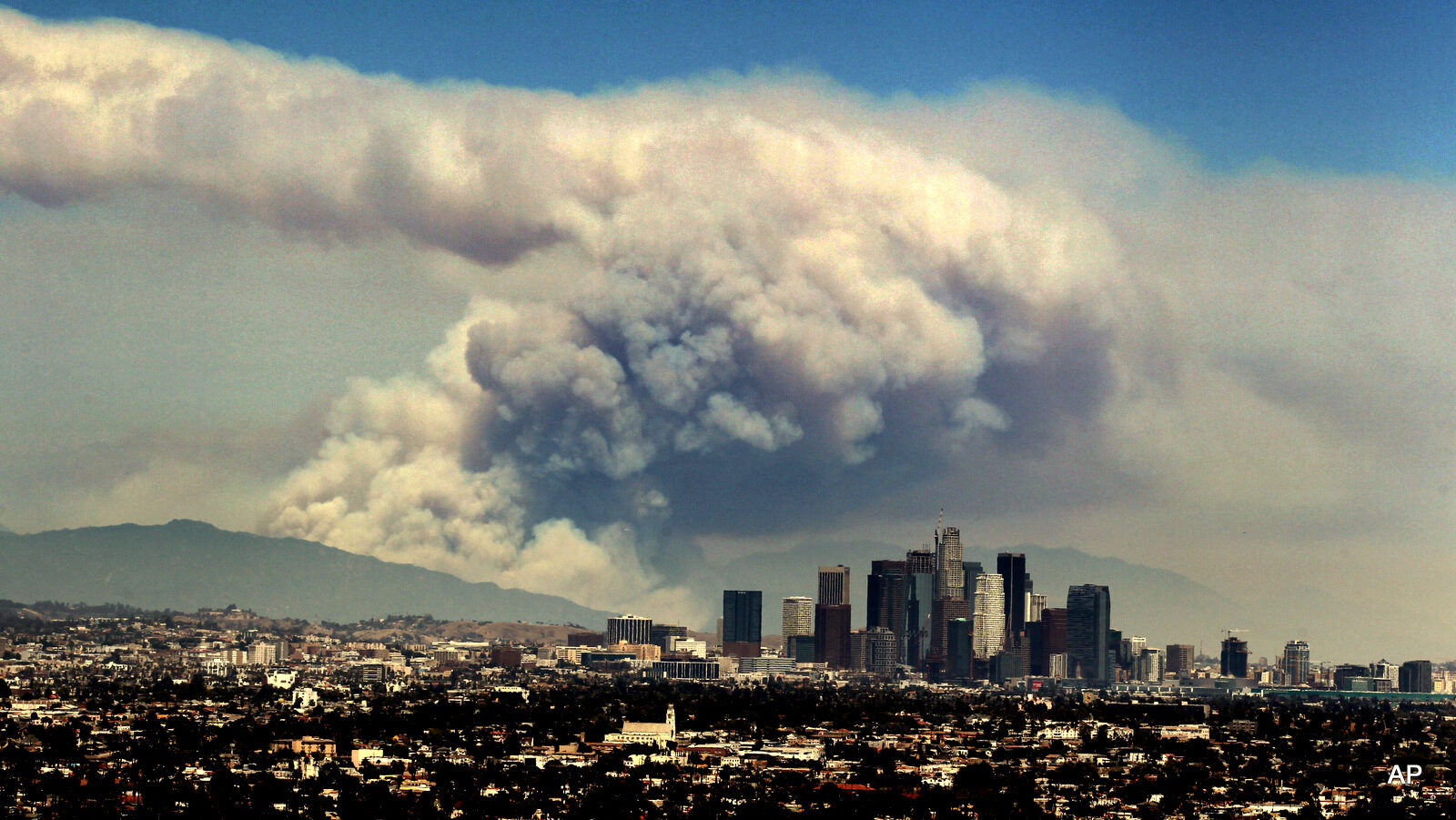 Smoke from wildfires burning in Angeles National Forest fills the sky behind the Los Angeles skyline on Monday, June 20, 2016. The wildfires several miles apart devoured hundreds of acres of brush on steep slopes above foothill suburbs erupted in Southern California as an intensifying heat wave stretching from the West Coast to New Mexico blistered the region with triple-digit temperatures.