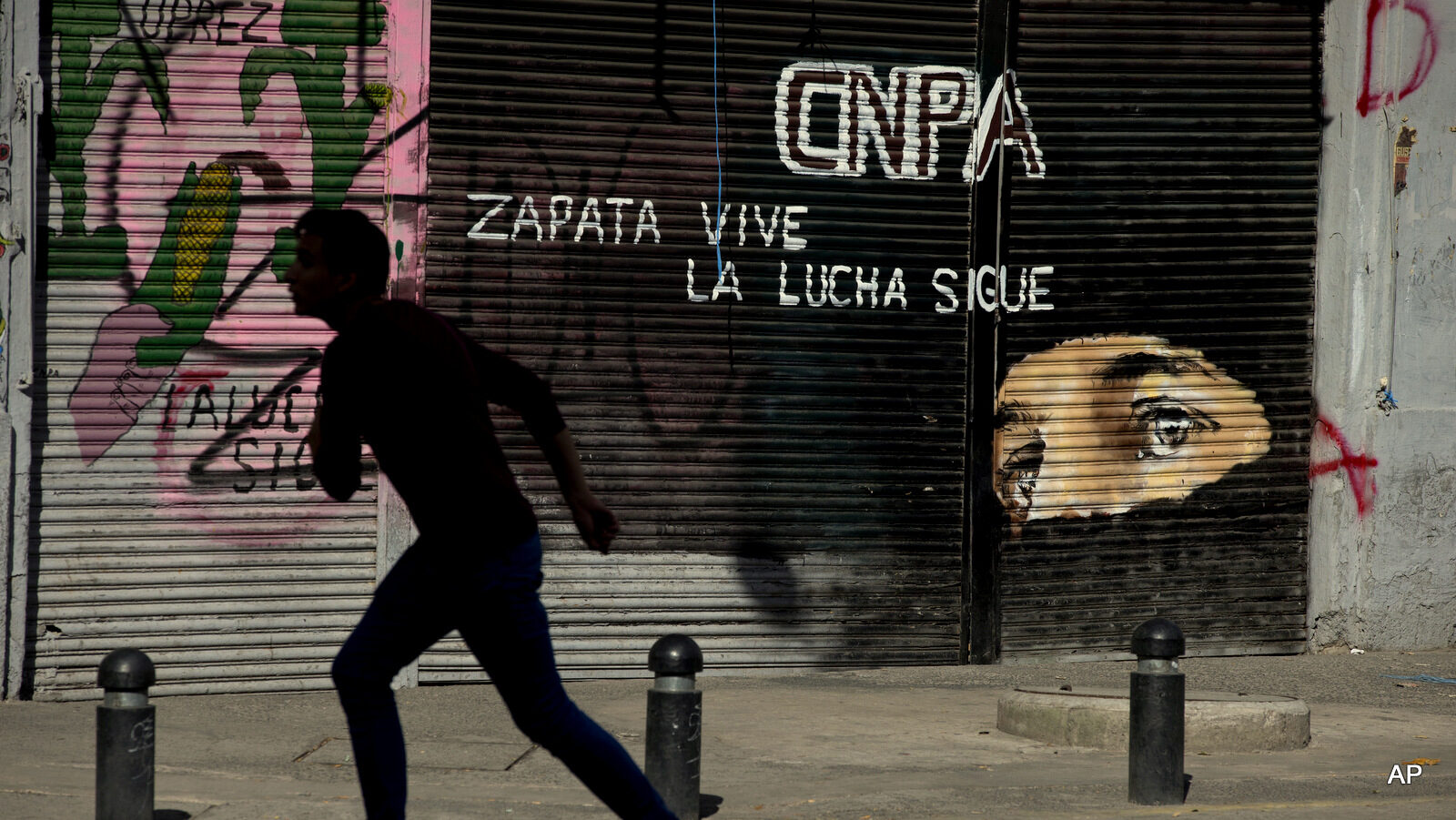 A boy runs past a mural of rebel leader Sub Comandante Marcos with the slogan in Spanish "Zapata lives. The struggle continues," in Mexico City, Wednesday, June 22, 2016. A group of protesting teachers accompanied by a mediation commission were meeting Wednesday evening with Interior Secretary Miguel Angel Osorio Chong. The negotiations between the striking radical teachers and the government come three days after a clash between protestors and police in Oaxaca state left eight dead and more than 100 injured.