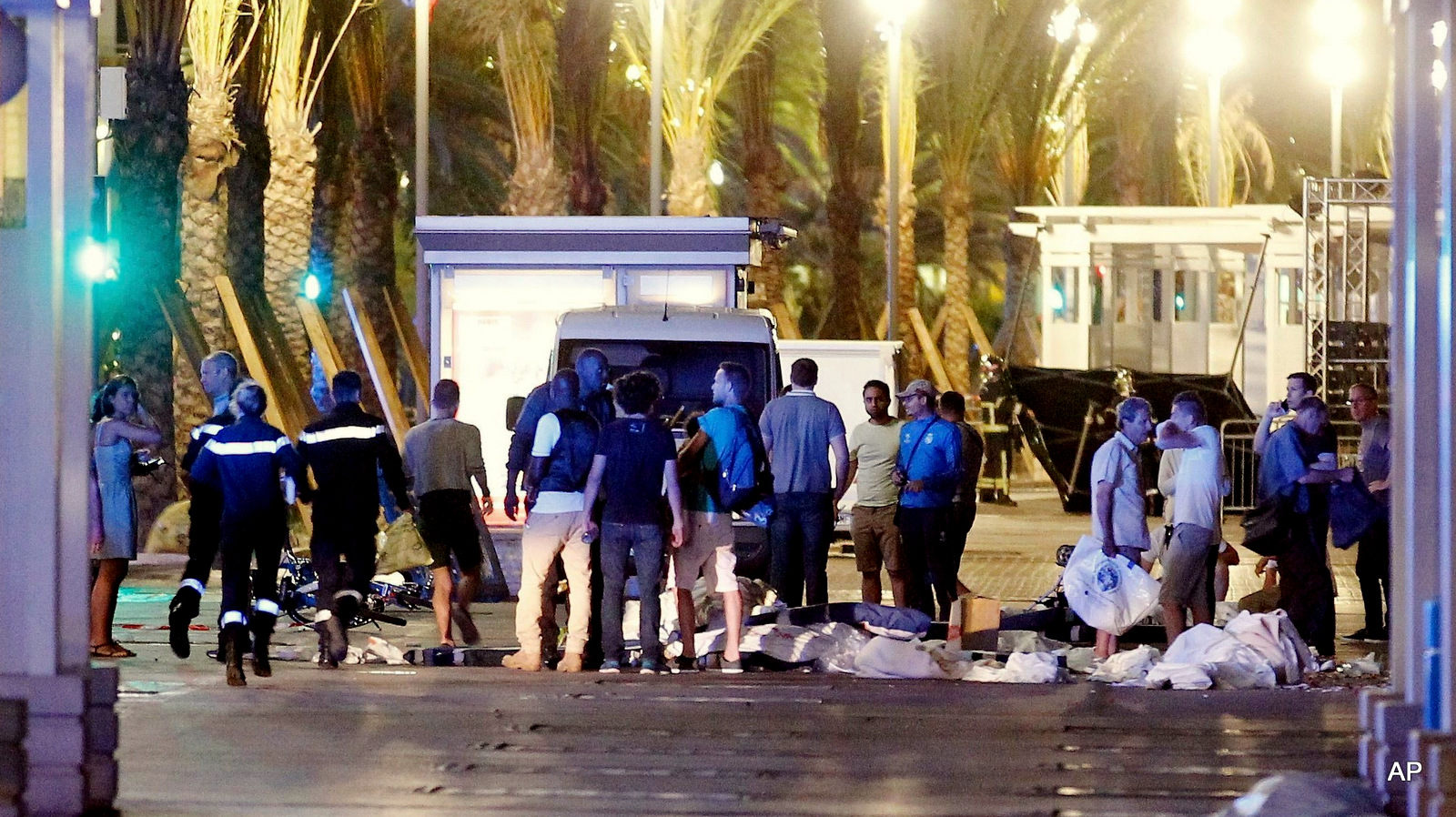 People stand next to covered bodies in the early hours of Friday, July 15, 2016, on the Promenade des Anglais in Nice, southern France.  