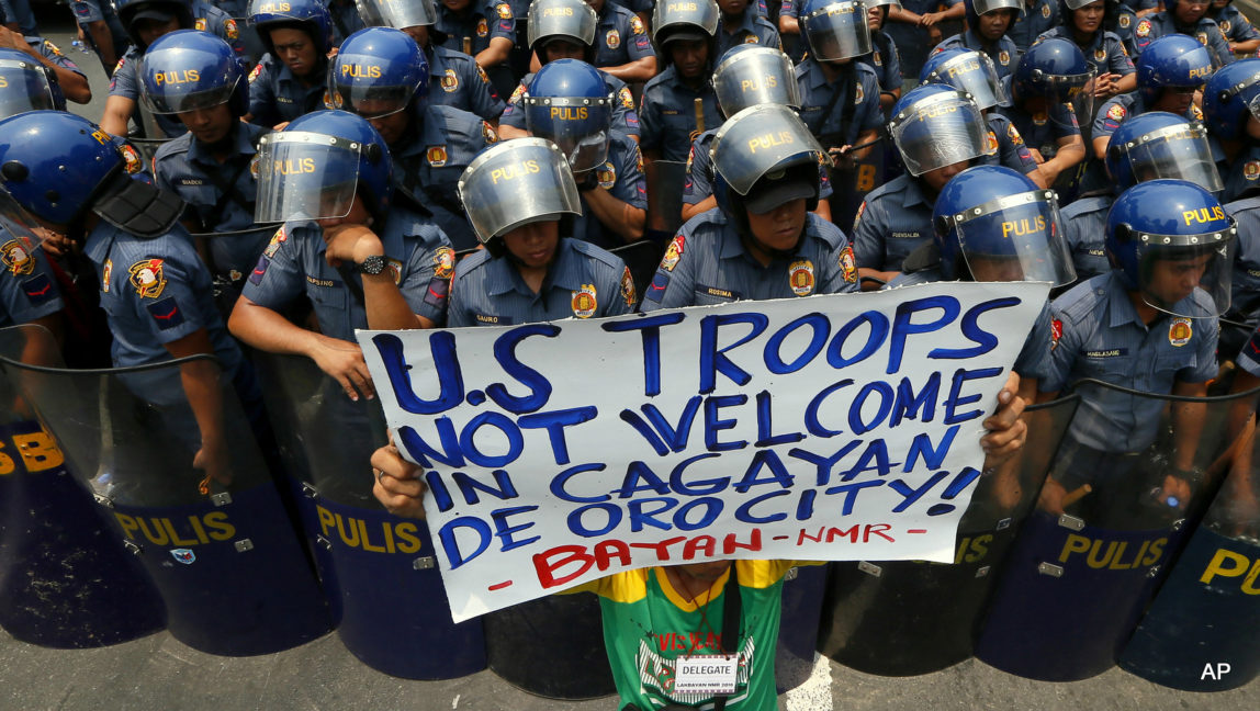 A protester displays a placard in front of riot police during a rally at the US Embassy to protest the visit of U.S. Secretary of State John Kerry Wednesday, July 27, 2016, in Manila, Philippines. The protesters are calling for the pullout of U.S. troops in the country under the Enhanced Defense Cooperation Agreement or EDCA which was entered into by the Philippines and U.S. militaries.