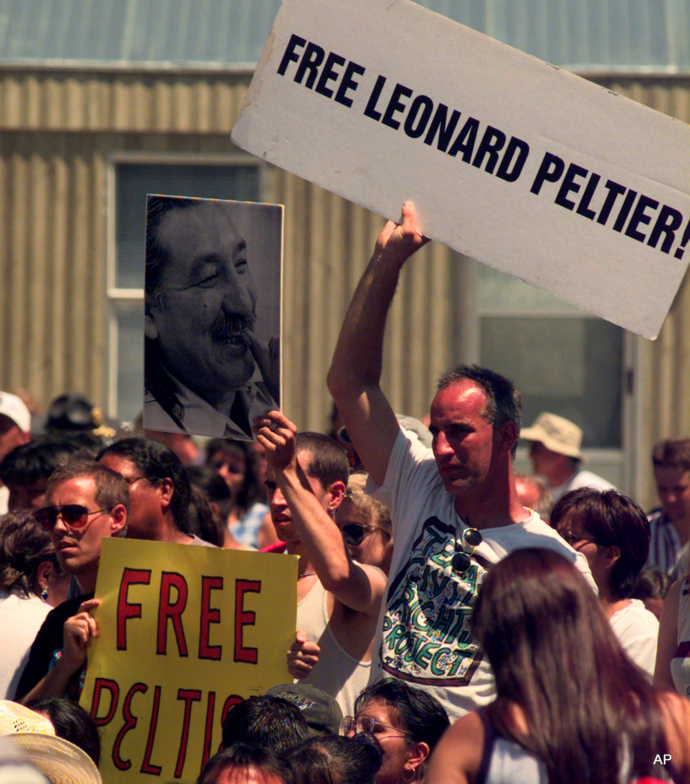 A group of protesters raise signs and a photo in support of Leonard Peltier during President Clinton's speech Wednesday, July 7, 1999 at Pine Ridge High School in Pine Ridge, S.D., on the Pine Ridge Indian Reservation