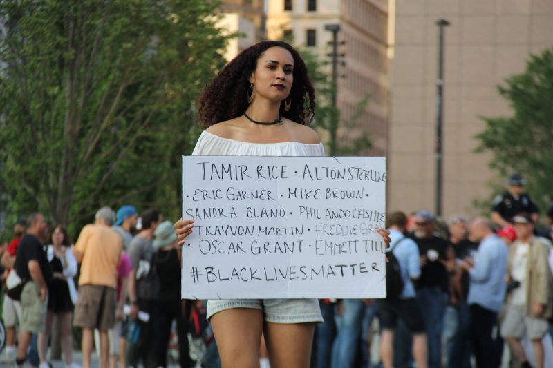 Near the 2016 Republican National Convention in Cleveland, Ohio, a woman holds a sign that reads #BlackLivesMatter along with the names of black people killed by police. (MintPress News / Desiree Kane)