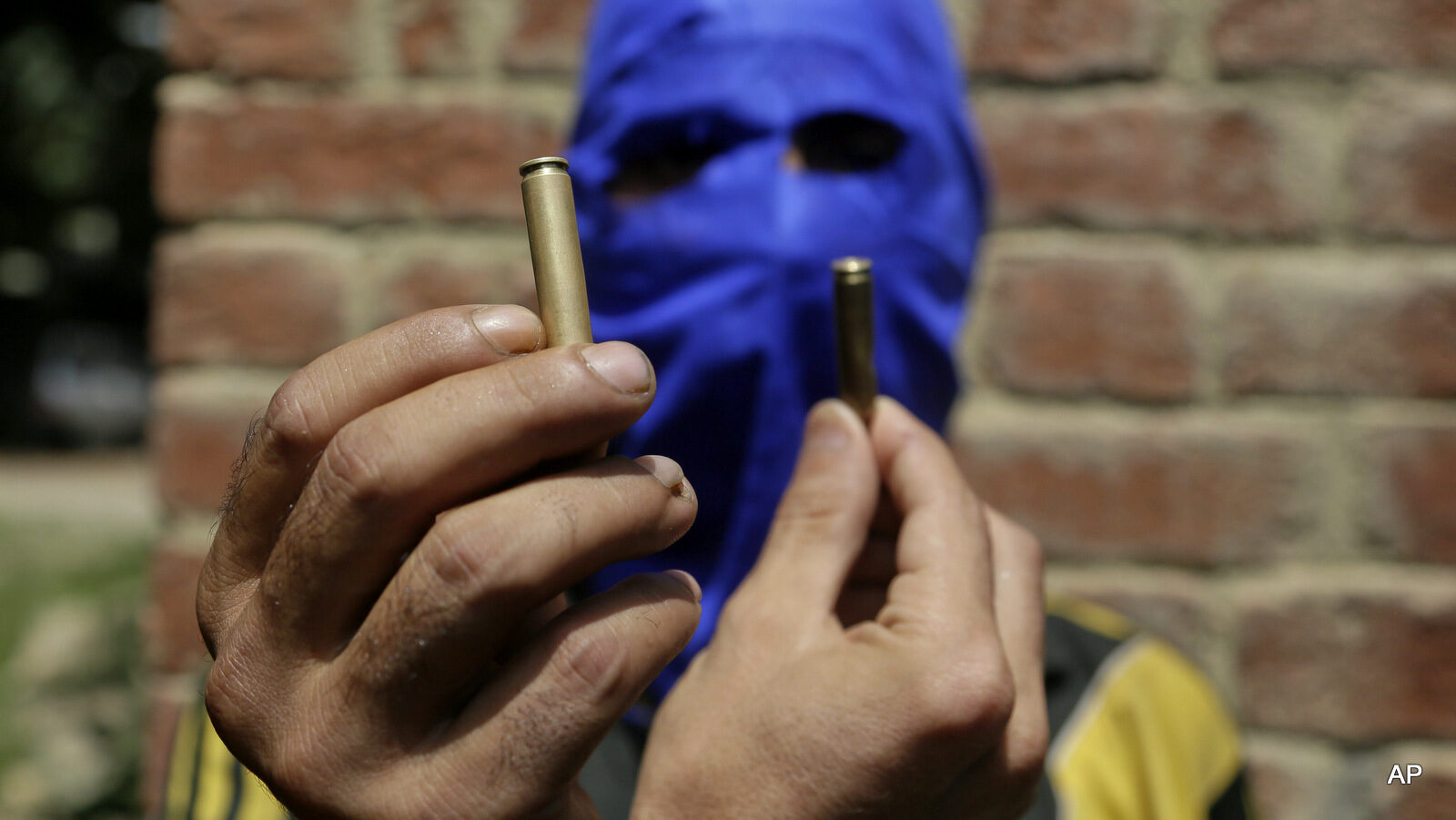 A masked Kashmiri youth shows empty bullet cartridges fired by Indian forces during a joint funeral of four civilians at Aripanthan village, west of Srinagar, Indian occupied Kashmir, Tuesday, Aug.16, 2016. Government forces in Indian-controlled Kashmir shot and killed four civilians and injured at least 15 others Tuesday as clashes intensified with anti-India protesters in the troubled region, police said.
