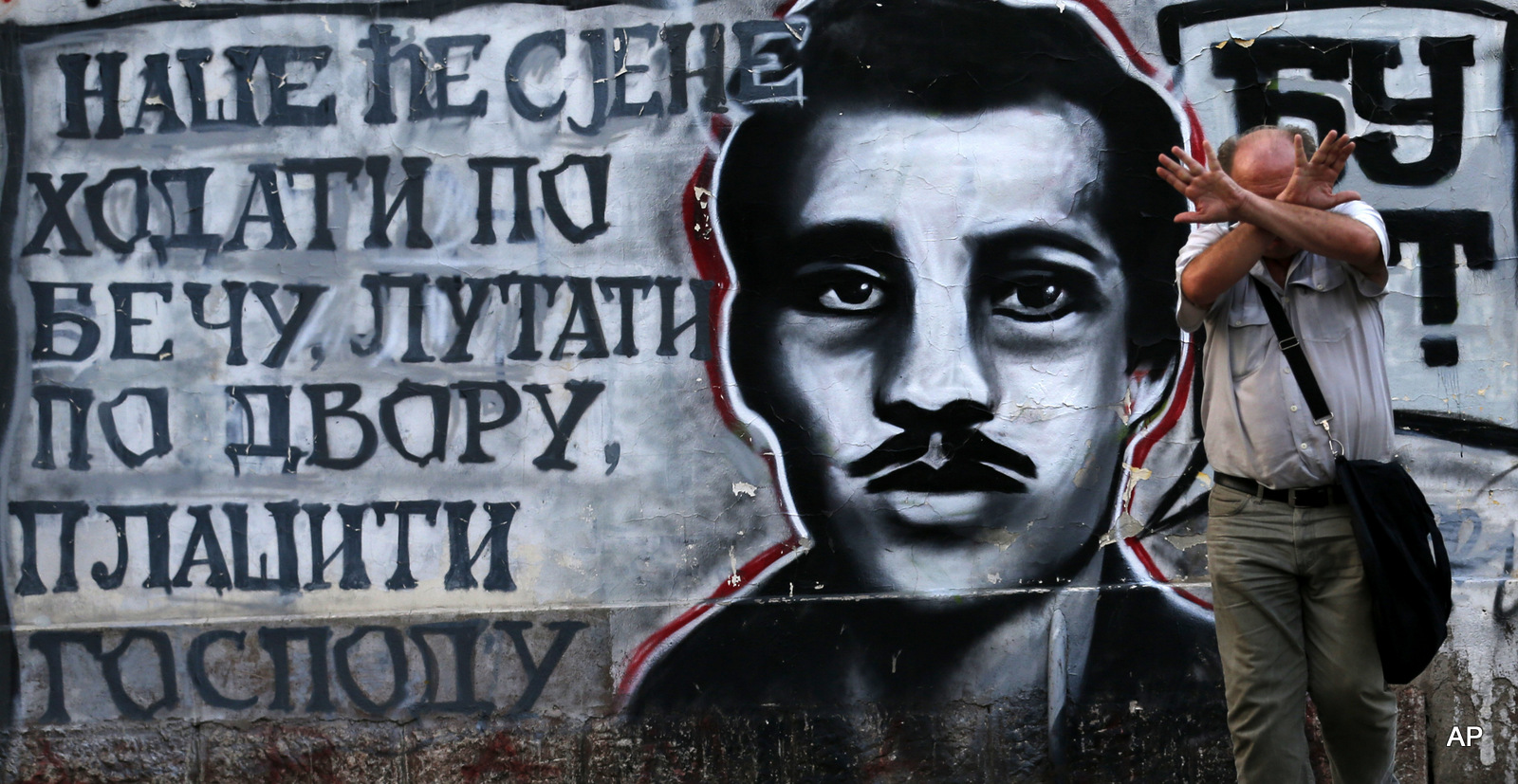 A man covers his face by graffiti on a wall showing Gavrilo Princip, the Bosnian-Serb nationalist who assassinated Archduke Franz Ferdinand in 1914, in Belgrade, Serbia, Tuesday, Aug. 30, 2016. On the left side are written the words that, by the legend, Princip inscribed on the wall of his cell shortly before his death: ''Our shadows will walk through Vienna, wander the palace, frighten the lords.''