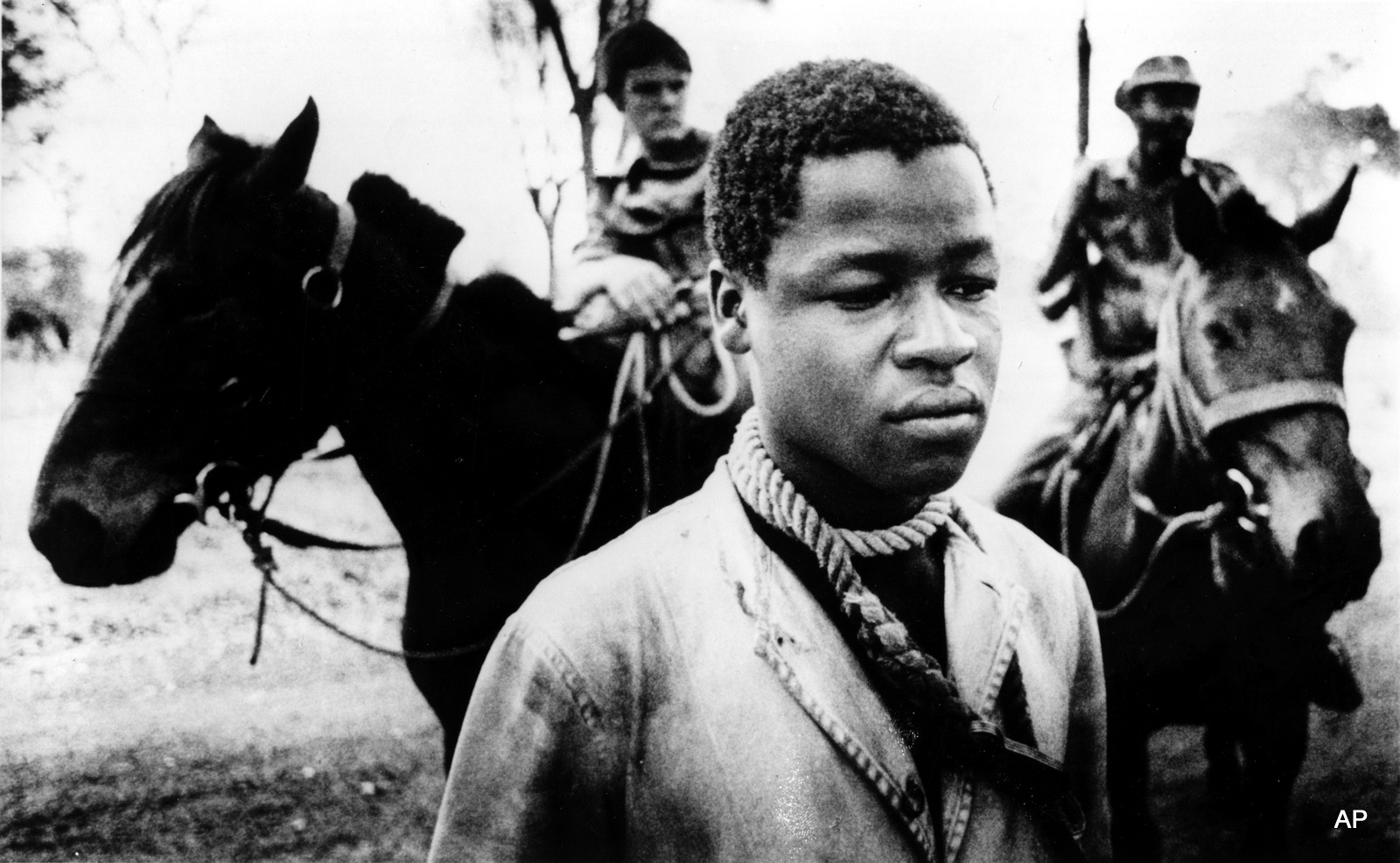 A black Rhodesian prisoner stands with a rope tied around his neck, to prevent escape, placed there by Rhodesian cavalrymen, background, who detain him for questioning in Lupane, Southern Rhodesia in Sept. 1977. Rhodesia's white-dominated government is countering black Rhodesian guerrilla activities with militant armed forces.
