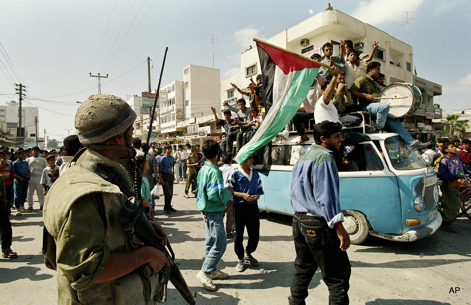 An Israeli soldier looks on as jubilant Palestinians ride on a truck celebrating the signing of the Israel-PLO agreement, May 4, 1994 in Gaza City, Gaza.