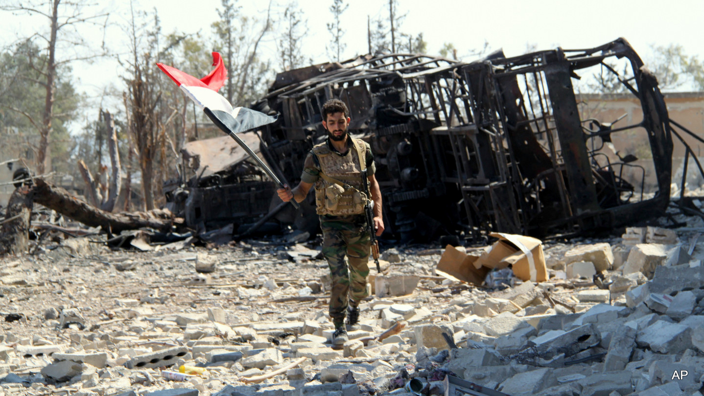 A Syrian soldier carries Syria's national flag after successfully routing rebels from the Aleppo Military Academy in Aleppo, Syria. Sept. 05, 2016.