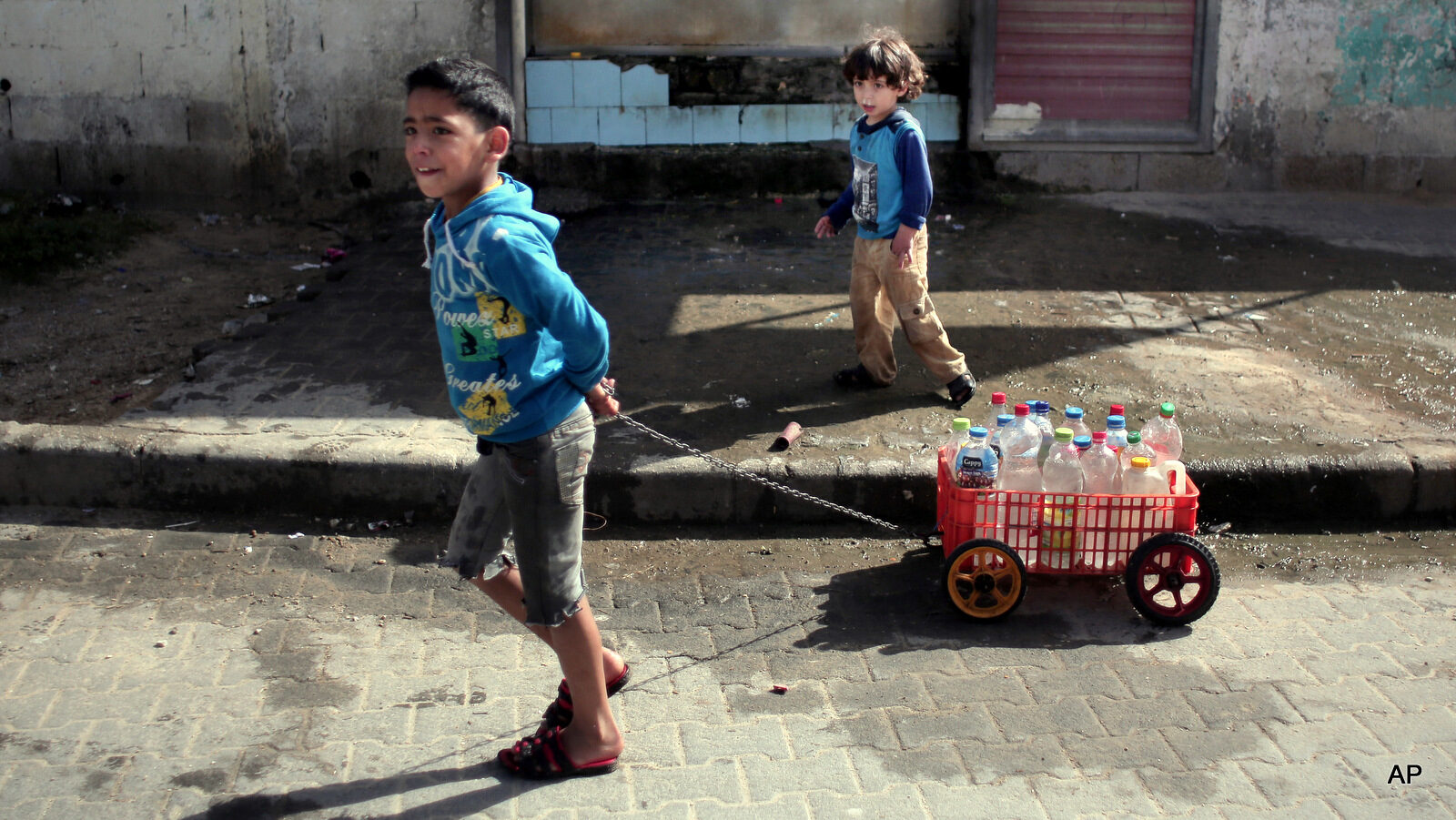 In this Saturday, April 16, 2016 photo, A Palestinian boy uses a homemade wagon made from a plastic crate to wheel bottles full of drinking water in front of a water supply station in Khan Younis refugee camp, southern Gaza Strip. Poor sewage treatment is a feature of life in Gaza, a result of infrastructure damaged during Israel's bombing campaigns and ongoing blockade.