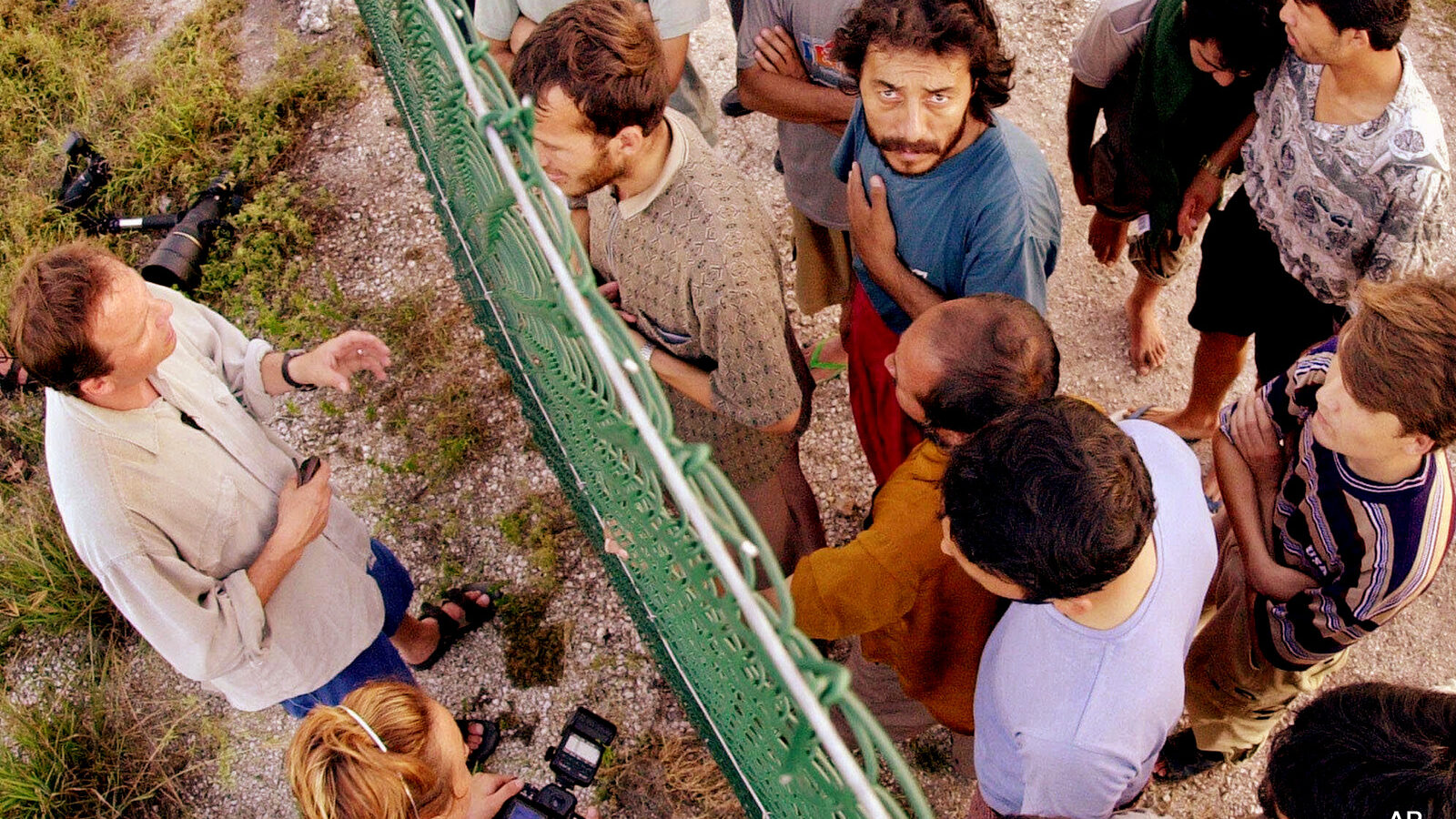In this Sept. 19, 2001, file photo, refugees, right, gather on one side of a fence to talk with international journalists about their journey that brought them to the Island of Nauru. Human rights groups accused Australia on Wednesday, Aug. 3, 2016, of deliberately ignoring the abuse of asylum seekers being held at the remote Pacific island detention camp in a bid to deter future refugees from trying to reach the country by boat.