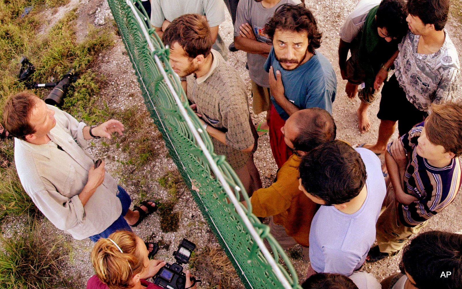 In this Sept. 19, 2001, file photo, refugees, right, gather on one side of a fence to talk with international journalists about their journey that brought them to the Island of Nauru. Human rights groups accused Australia on Wednesday, Aug. 3, 2016, of deliberately ignoring the abuse of asylum seekers being held at the remote Pacific island detention camp in a bid to deter future refugees from trying to reach the country by boat. 