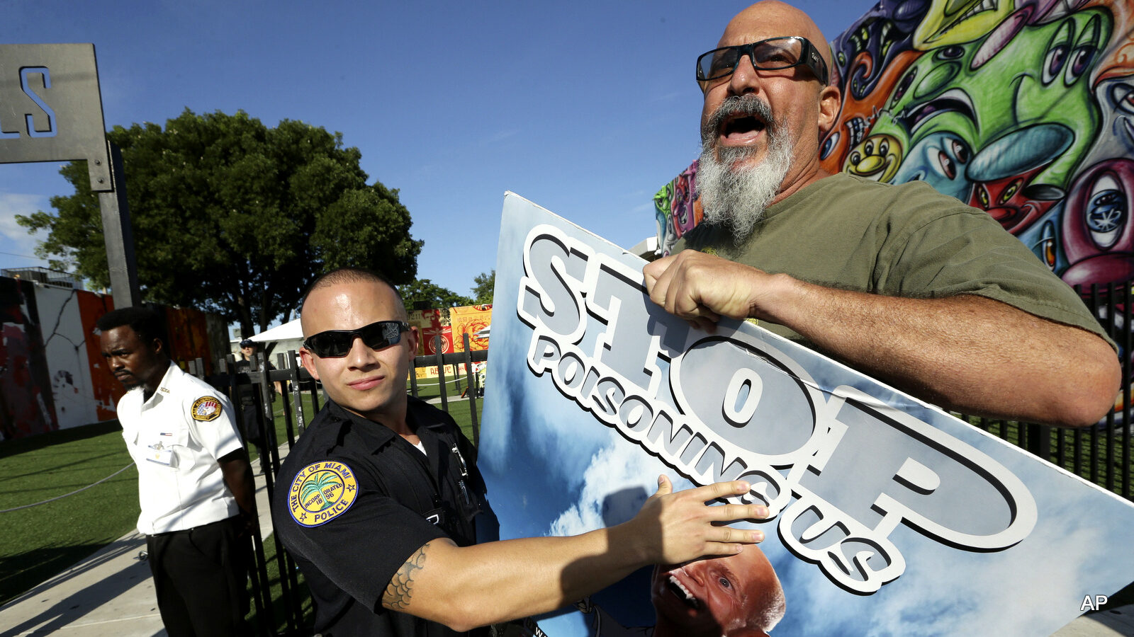 A Miami police officer holds back protestor Judd Allison, right, as Florida Gov. Rick Scott leaves a news conference at Wynwood Walls, Monday, Sept. 19, 2016, in the Wynwood neighborhood of Miami. The governor said the arts district is no longer considered a zone of active Zika transmission. It has been 45 days since the last Zika detection. Allison was protesting the use of the pesticide naled, which was used in the area to combat Zika.
