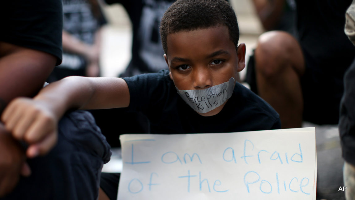 A young boy holds his fist up while wearing tape over his mouth during a Black Lives Matter protest at an entrance to Lenox Square Mall in Atlanta, Saturday, Sept. 24, 2016, in response to the police shooting deaths of Terence Crutcher in Tulsa, Okla. and Keith Lamont Scott in Charlotte, N.C. The Black Lives Matter chapter of Atlanta is boycotting major retailers following the recent police shooting deaths involving black men.