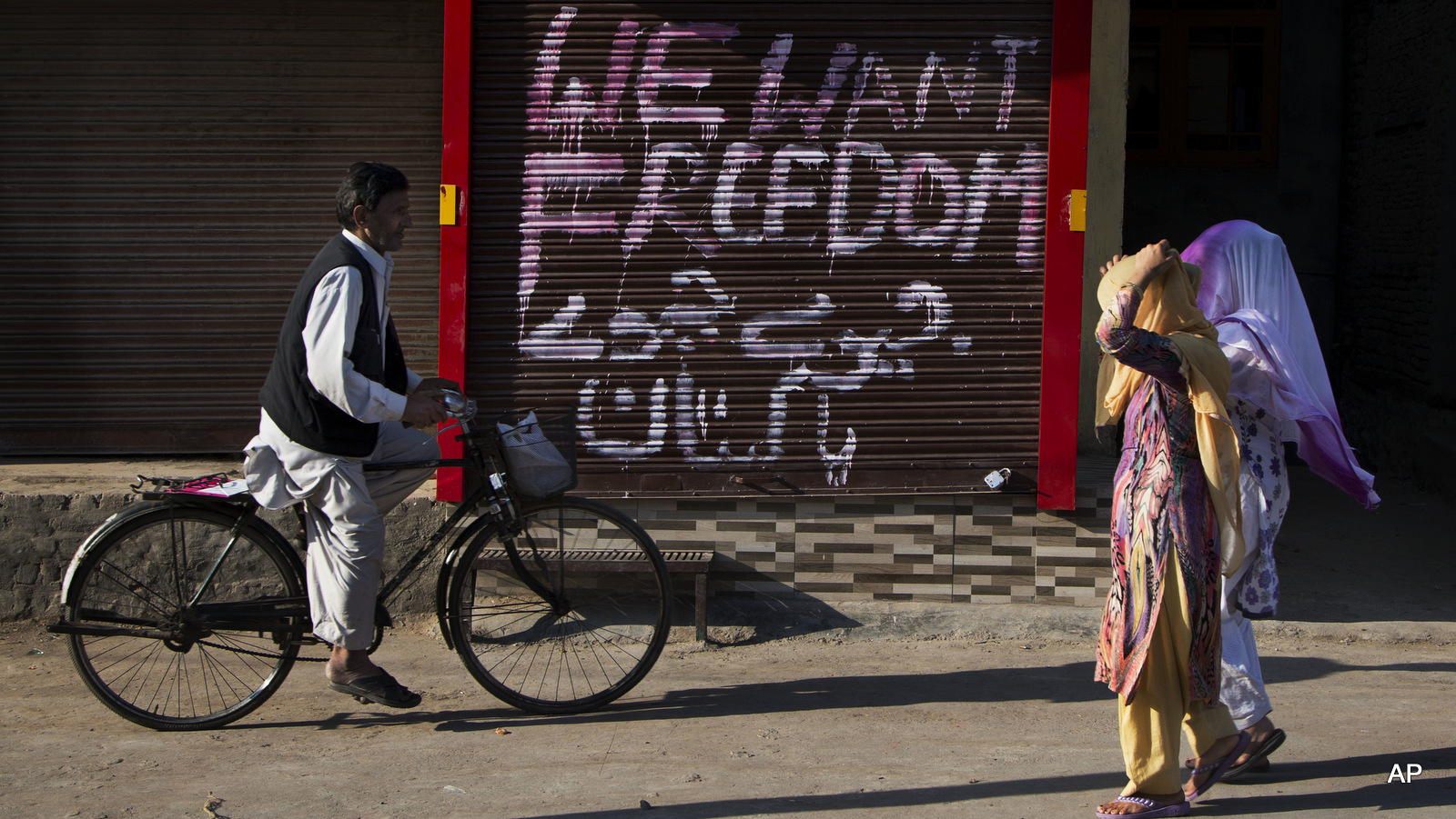 Kashmiri women walk past a closed market with graffiti painted on the shutter of a shop in Urdu that reads "Long live Pakistan" in Srinagar, Indian occupied Kashmir, Thursday, Sept. 29, 2016.