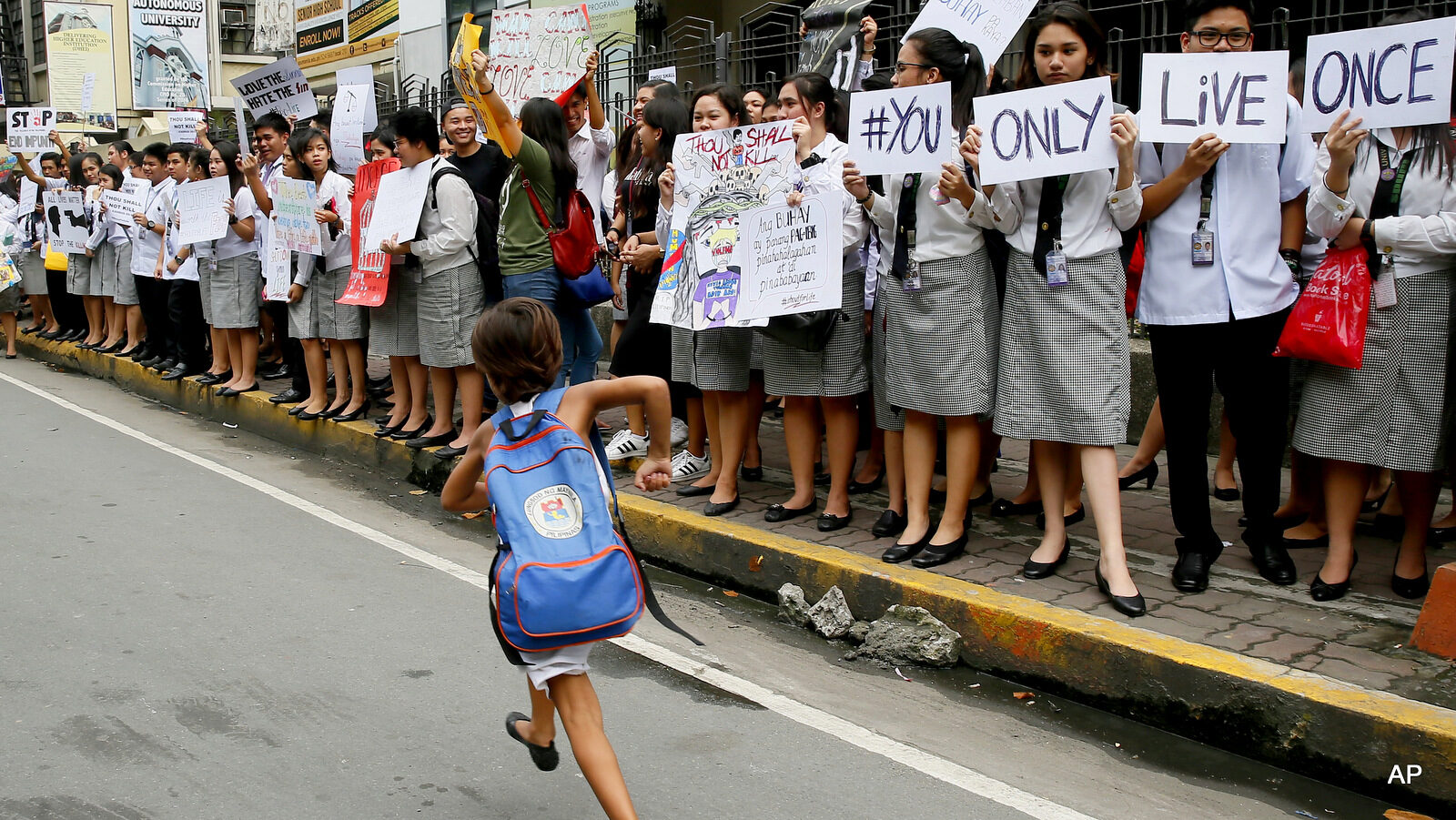 A school girl runs in front of students from St. Paul's University, a Roman Catholic school, as they come out from their campus to protest the killings being perpetrated in the unrelenting "War on Drugs" campaign of President Rodrigo Duterte, Friday, Sept. 30, 2016 in Manila, Philippines. Duterte raised the rhetoric over his bloody anti-crime war to a new level Friday, comparing it to Hitler and the Holocaust and saying he would be "happy to slaughter" 3 million addicts. Duterte issued his latest threat against drug dealers and users early Friday on returning to his hometown in southern Davao city after visiting Vietnam, where he discussed his anti-drug campaign with Vietnamese leaders and compared notes on battling the problem.