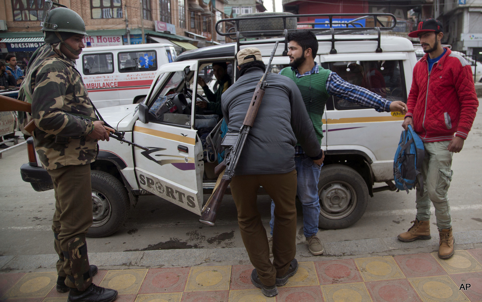 An Indian police man frisks a Kashmiri youth as an Indian paramilitary soldier, left, stands guard at a temporary checkpoint in Srinagar, Indian occupied Kashmir, Wednesday, Nov. 4, 2015.