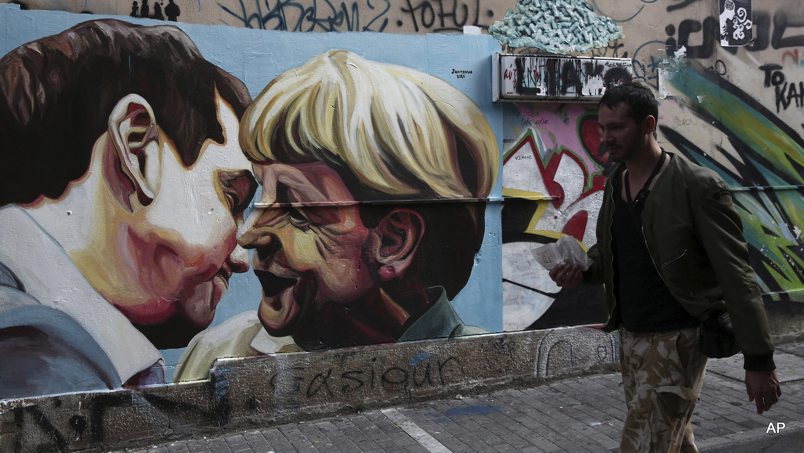 FILE - In this Sunday, Oct. 18, 2015 file photo, a man walks past street art depicting Greek Prime Minister Alexis Tsipras and German Chancellor Angela Merkel in Athens, Greece. Tsipras' decision to sign off on a bailout led to many in his left-wing Syriza party to quit in protest.