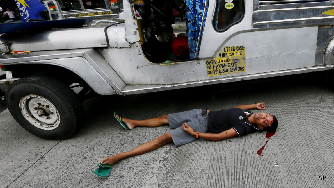 A bloodied protester lies next to a passenger vehicle after he was injured in a violent dispersal outside the U.S. Embassy in Manila, Philippines Wednesday, Oct. 19, 2016.