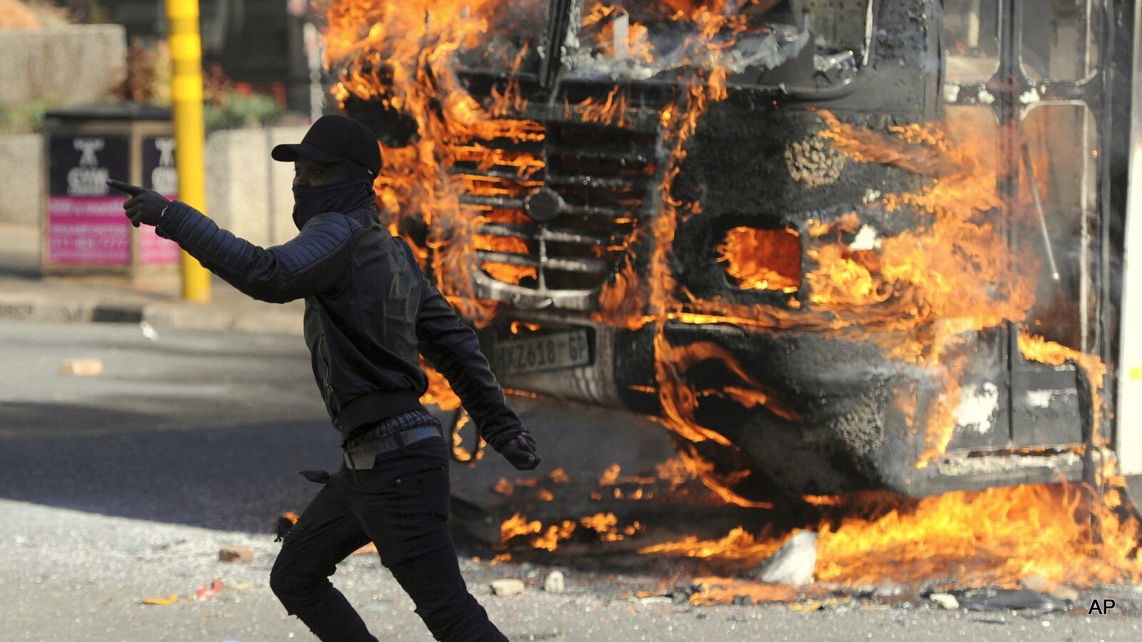 A protesting student runs past a burning bus off campus outside the University of the Witwatersrand in Johannesburg, South Africa on Monday, Oct. 10, 2016. Tear gas and water cannon were fired as hundreds of students protested at the university amid a bitter national dispute with university managers and the government over demonstrators' demands for free education, forcing student into the neighbouring city streets.