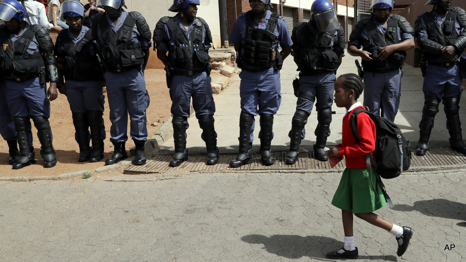 A young girl wearing school uniform, walks past riot police officers as they guard students from the University of the Witswatersrand outside the Hillbrow Magistrate’s Court in Johannesburg, South Africa, Wednesday, Oct. 12, 2016, protesting in support of their peers who were arrested earlier this week.