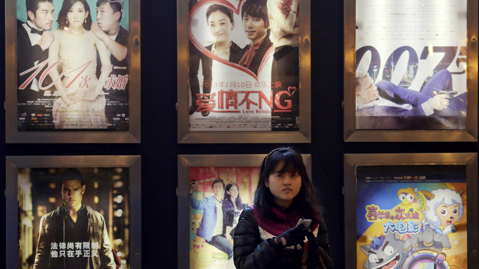 A woman stands in front of the advertisements of Chinese and foreign films on showing at a movie theater in Shanghai, China.