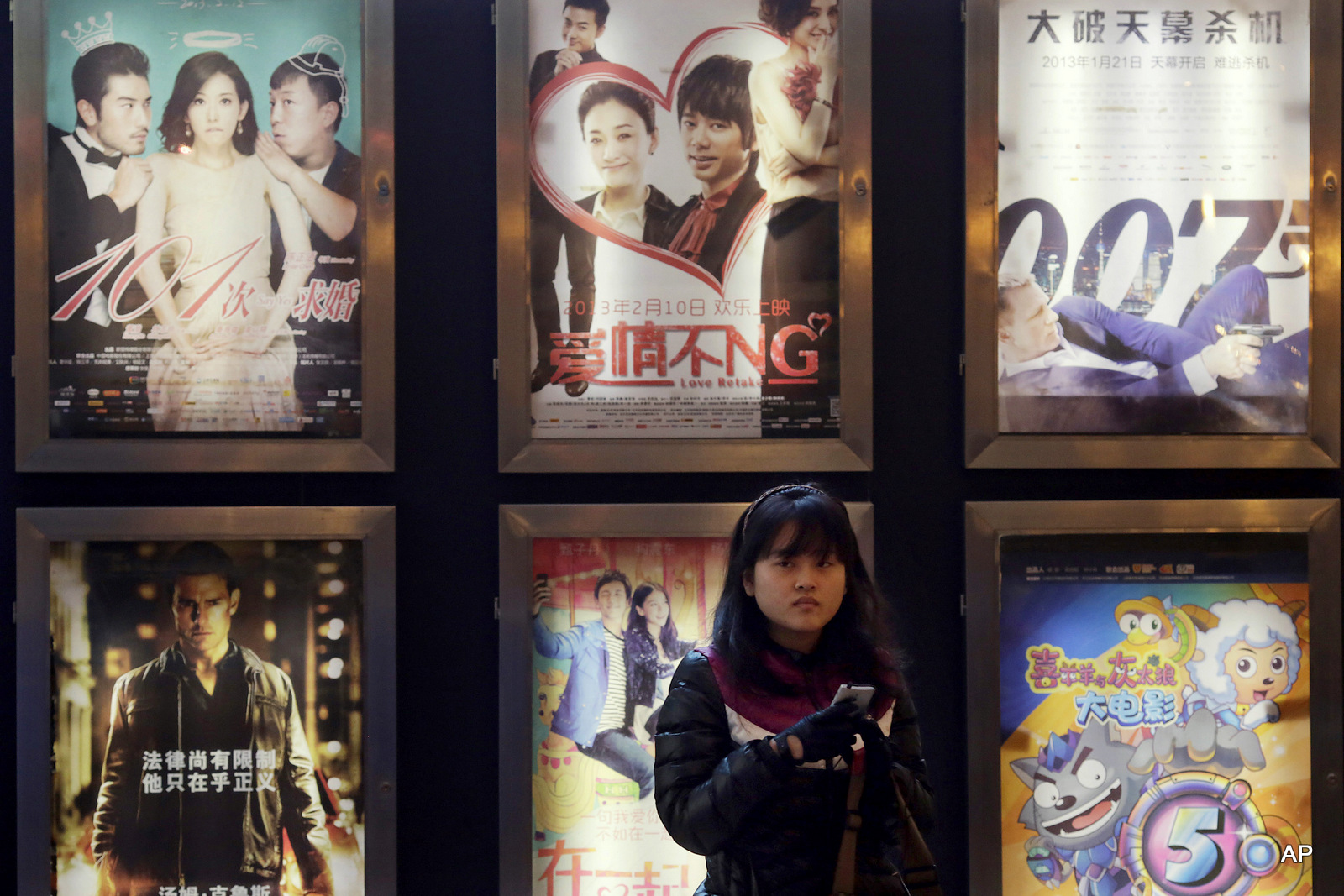 A woman stands in front of the advertisements of Chinese and foreign films on showing at a movie theater in Shanghai, China. 